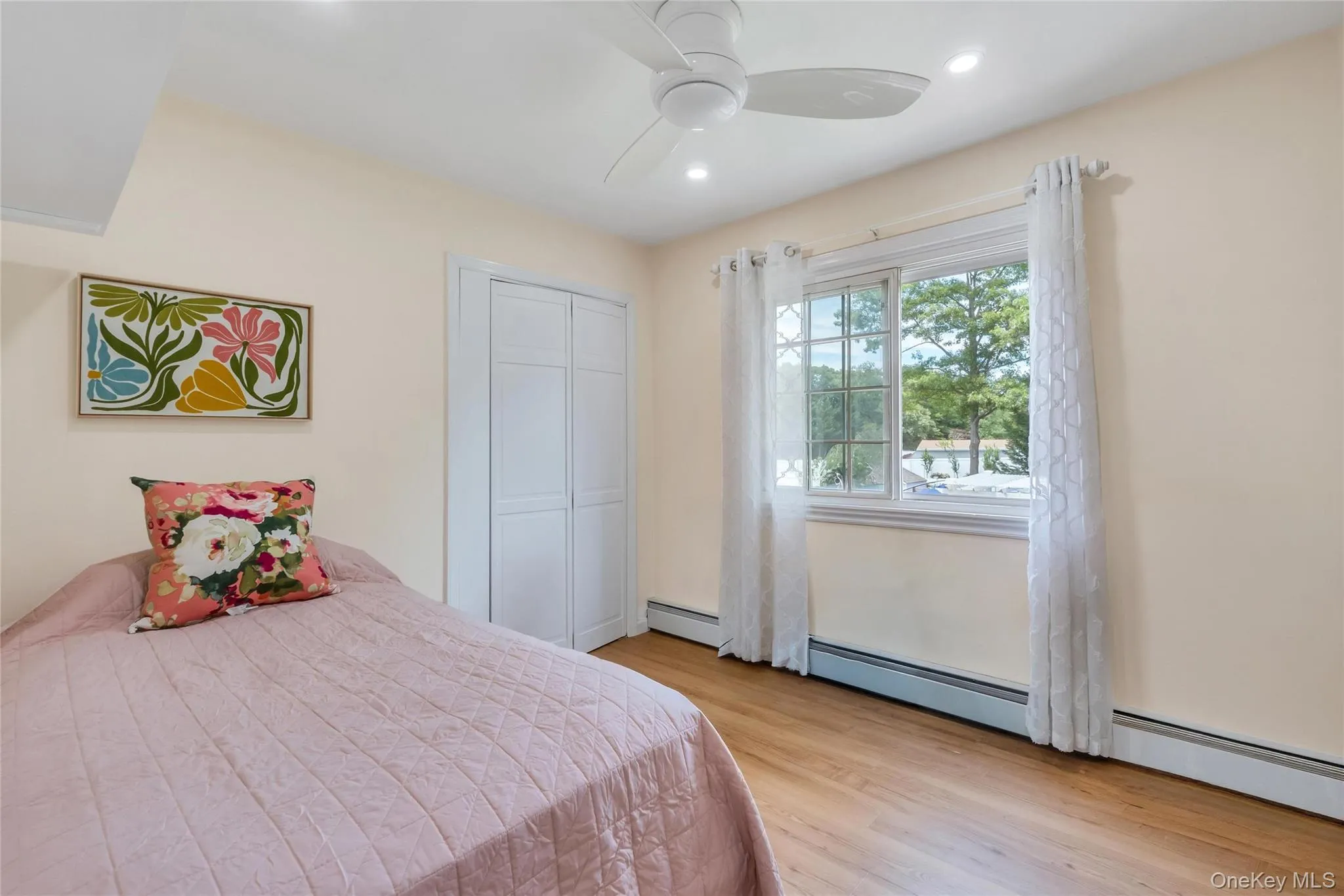 Bedroom featuring light-toned walls, wood-finish flooring, a double window with grid detailing, and a ceiling fan with integrated lighting Bedroom featuring light-toned walls, wood-finish flooring, a double window with grid detailing, and a ceiling fan with integrated lighting