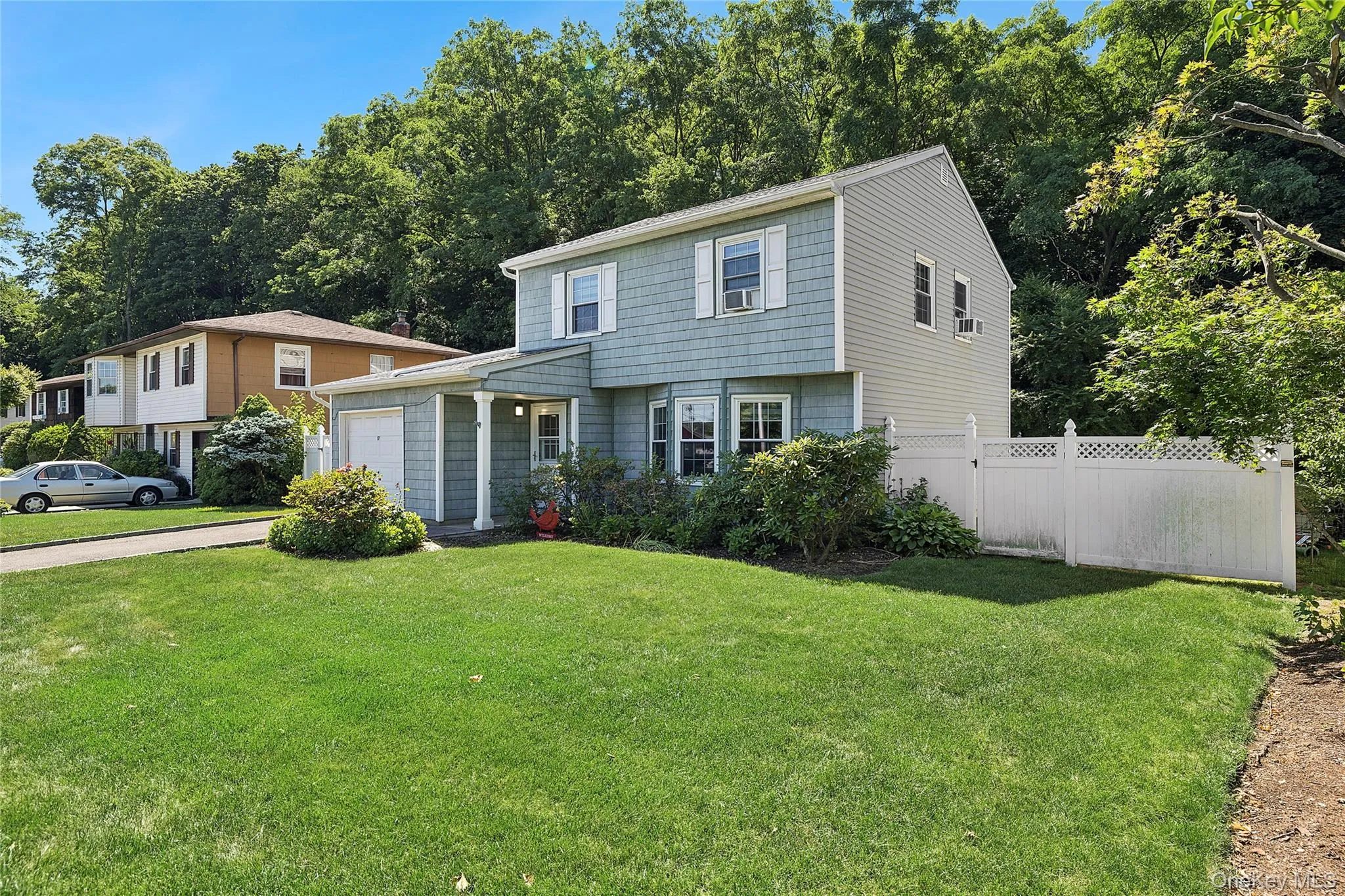 Split-level residence featuring gray siding with white trim, a single-car garage, and a white lattice fence Split-level residence featuring gray siding with white trim, a single-car garage, and a white lattice fence