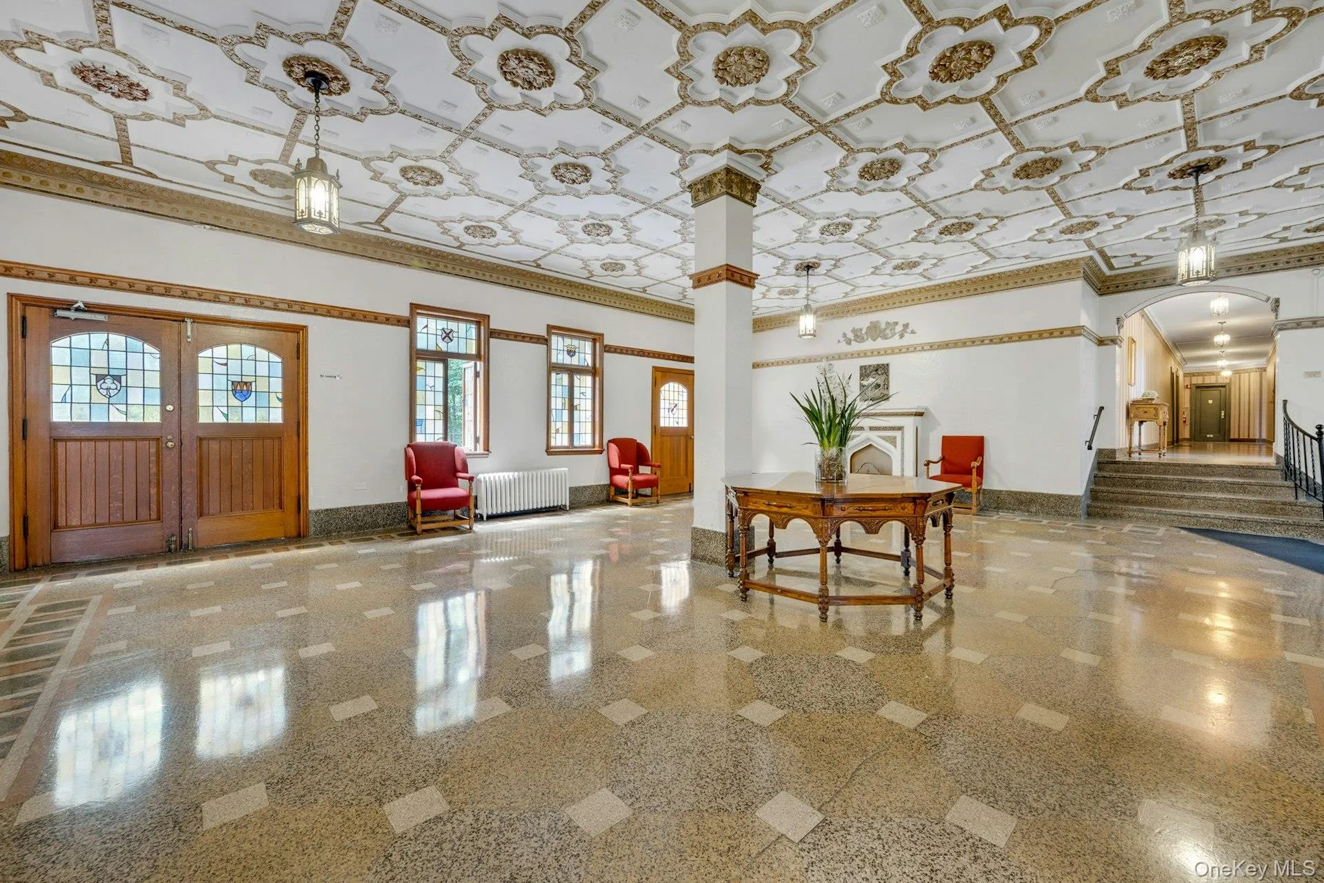 Lobby featuring an ornate coffered ceiling with decorative molding, polished terrazzo flooring, a decorative fireplace, and classic wood doors with stained glass inserts Lobby featuring an ornate coffered ceiling with decorative molding, polished terrazzo flooring, a decorative fireplace, and classic wood doors with stained glass inserts