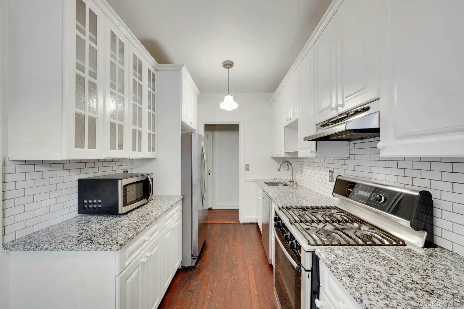 Galley kitchen featuring white cabinetry, granite countertops, subway tile backsplash, and stainless steel appliances Galley kitchen featuring white cabinetry, granite countertops, subway tile backsplash, and stainless steel appliances