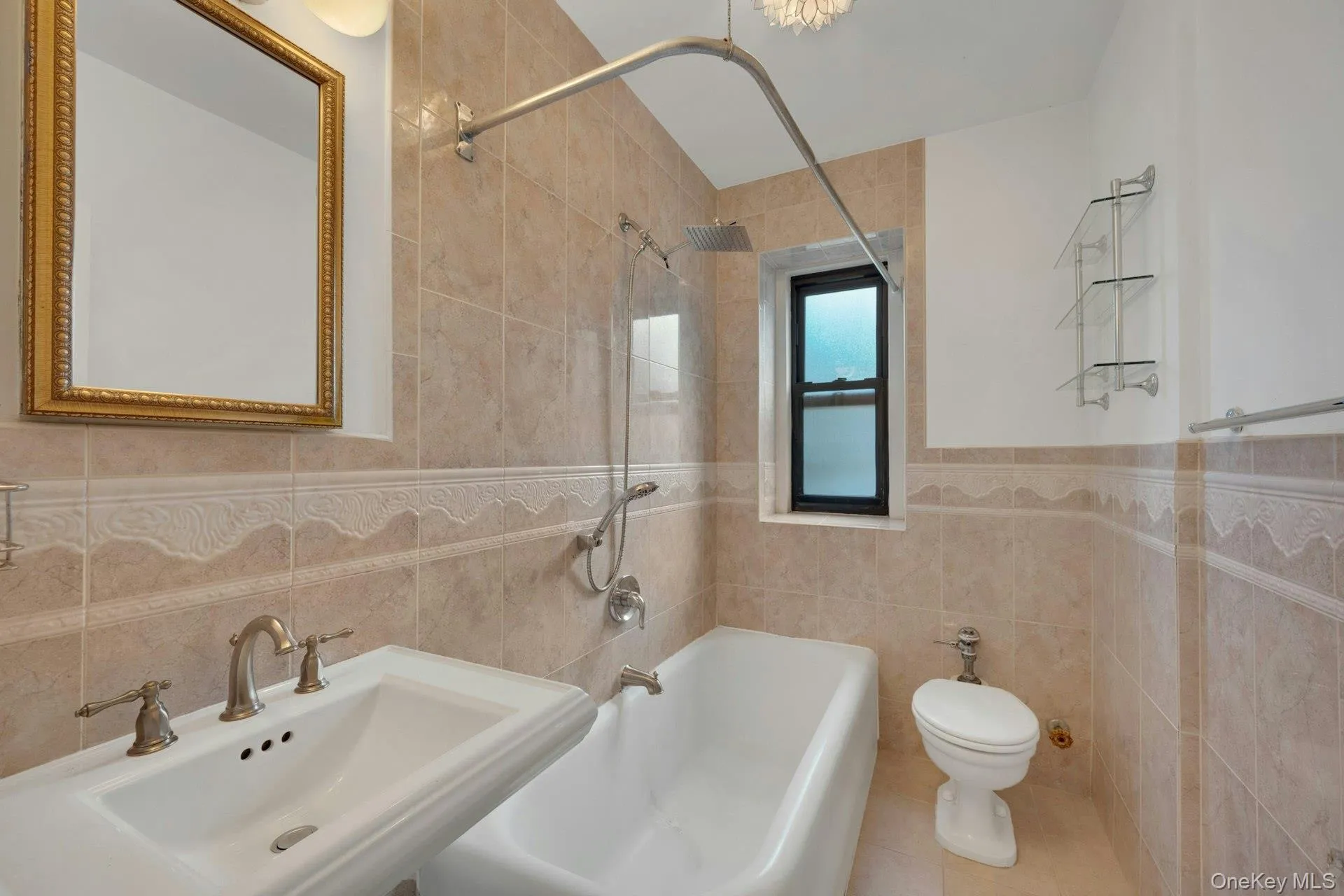 Bathroom featuring a pedestal sink with brass-finish faucet, a bathtub with a rainfall showerhead, and neutral-toned wall tiling with a decorative border Bathroom featuring a pedestal sink with brass-finish faucet, a bathtub with a rainfall showerhead, and neutral-toned wall tiling with a decorative border