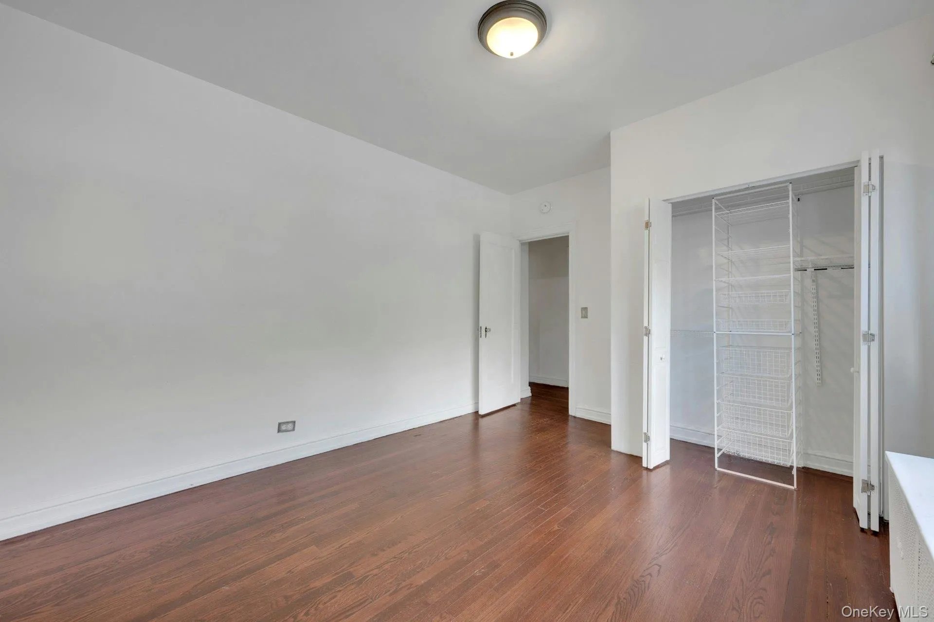 Room featuring wood-finish flooring, white walls, and a ceiling-mounted light fixture Room featuring wood-finish flooring, white walls, and a ceiling-mounted light fixture