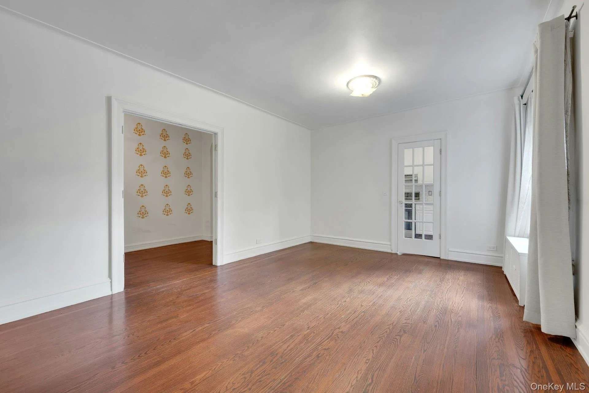 Spacious room featuring rich wood-finish flooring, white walls, and a ceiling-mounted light fixture Spacious room featuring rich wood-finish flooring, white walls, and a ceiling-mounted light fixture