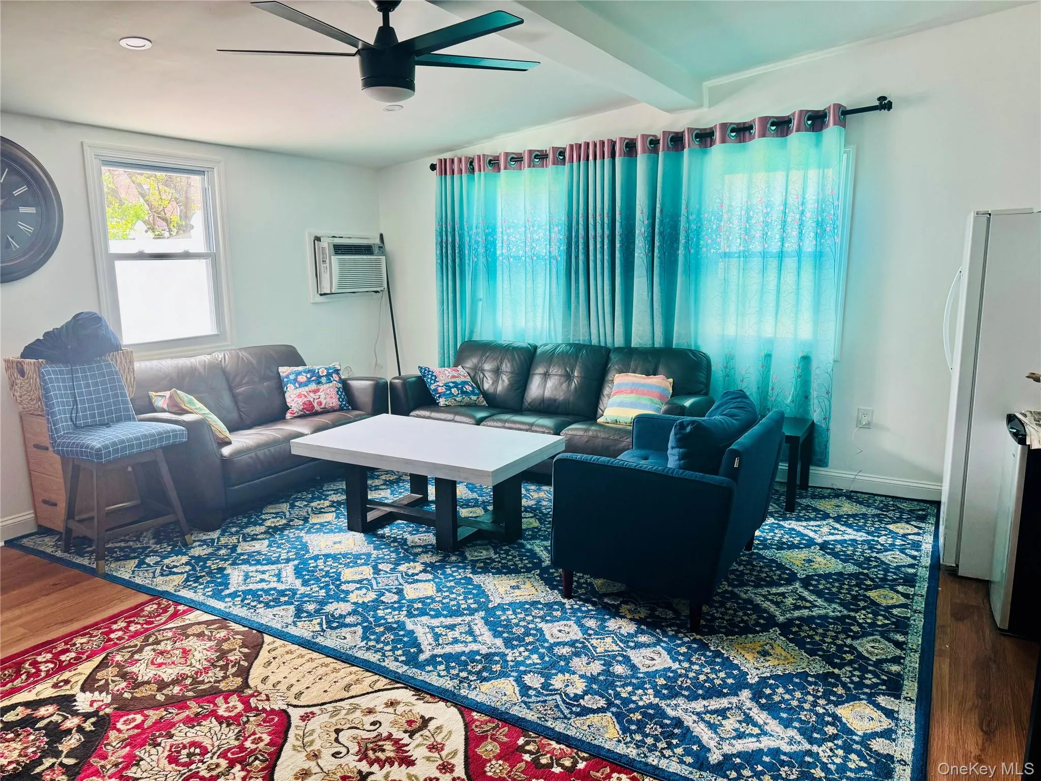 Living area featuring wood finished floors, ceiling fan, an AC wall unit, baseboards, and beam ceiling Living area featuring wood finished floors, ceiling fan, an AC wall unit, baseboards, and beam ceiling