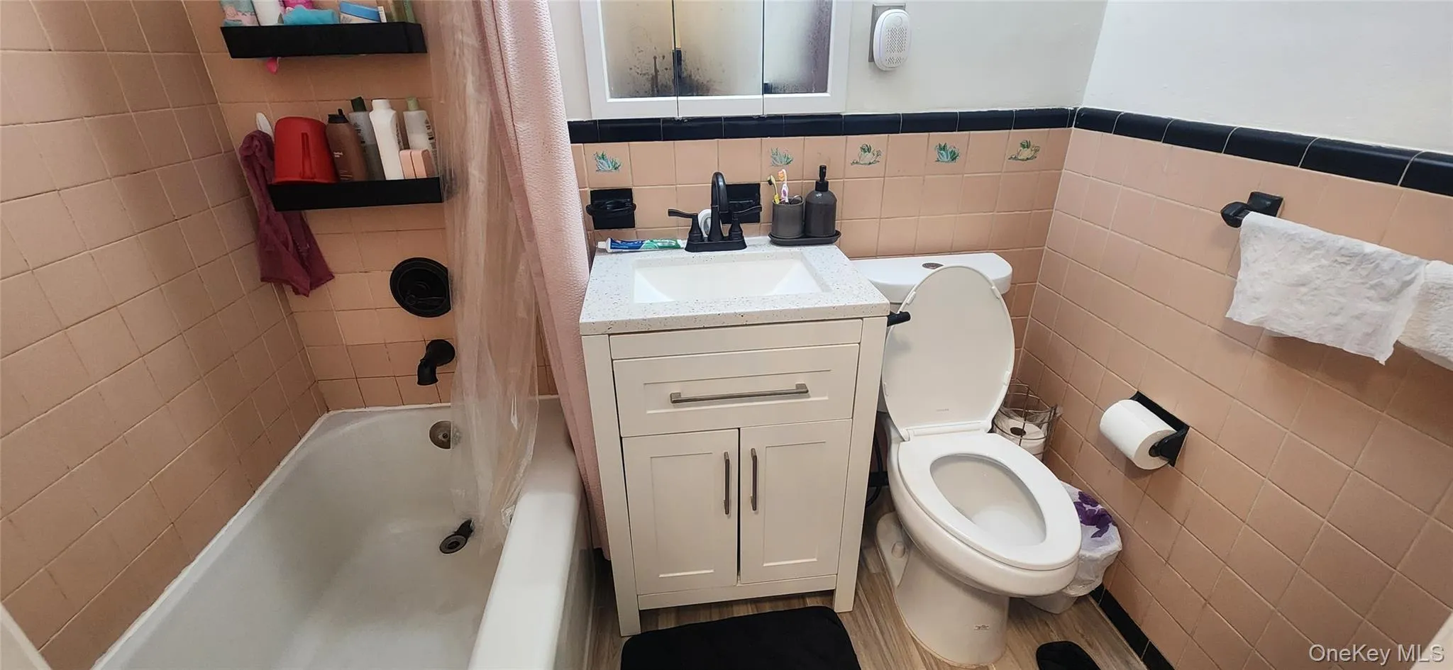 Full bath featuring tile walls, toilet, shower / bathtub combination with curtain, a wainscoted wall, and vanity Full bath featuring tile walls, toilet, shower / bathtub combination with curtain, a wainscoted wall, and vanity
