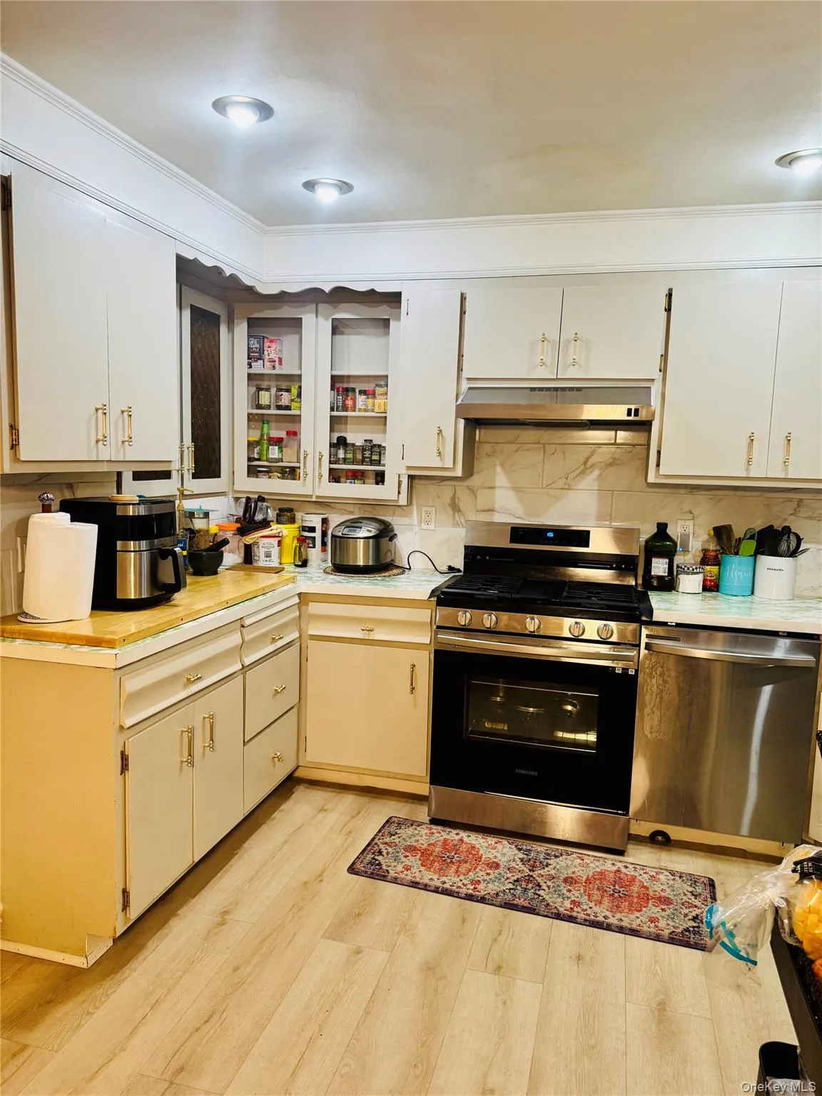 Kitchen featuring appliances with stainless steel finishes, light countertops, light wood-style floors, under cabinet range hood, and decorative backsplash Kitchen featuring appliances with stainless steel finishes, light countertops, light wood-style floors, under cabinet range hood, and decorative backsplash