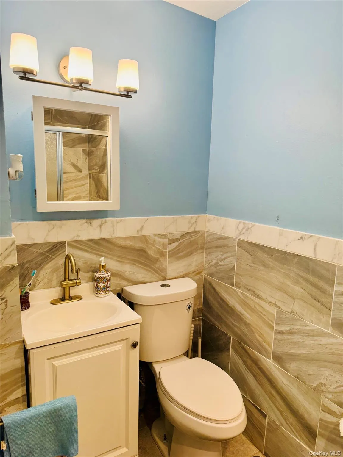 Full bath with tile walls, vanity, toilet, an enclosed shower, and a wainscoted wall Full bath with tile walls, vanity, toilet, an enclosed shower, and a wainscoted wall