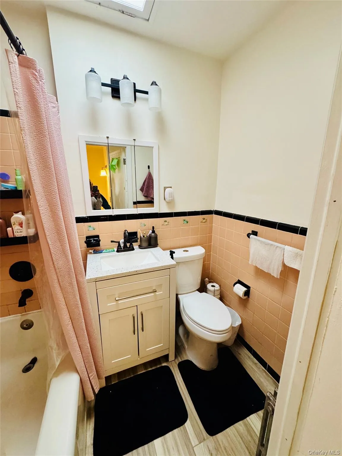 Bathroom featuring tile walls, toilet, a wainscoted wall, vanity, and shower / bath combo Bathroom featuring tile walls, toilet, a wainscoted wall, vanity, and shower / bath combo