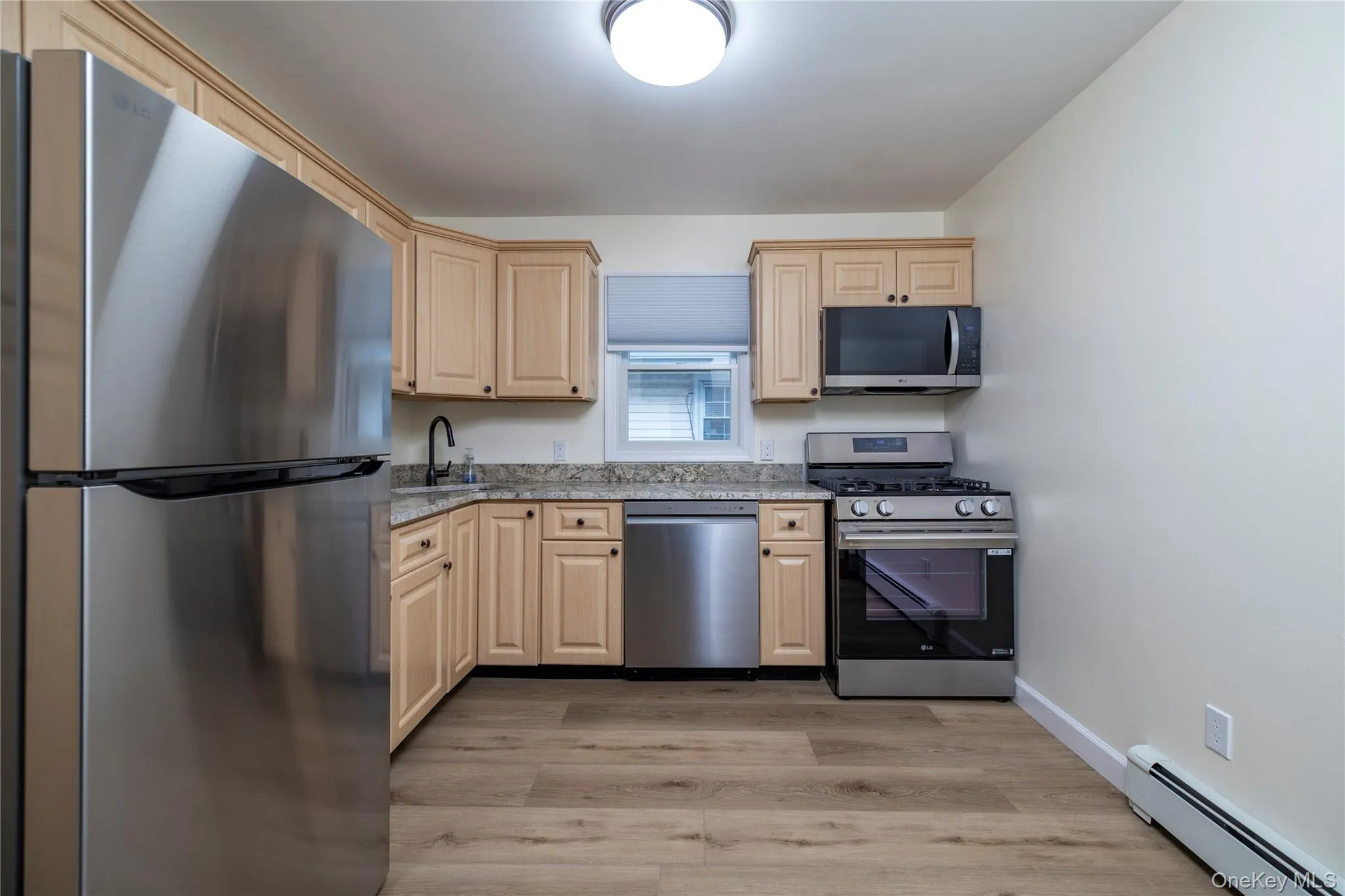 Kitchen with light wood cabinetry, granite-style countertops, and stainless steel appliances including a refrigerator, dishwasher, and range with an overhead microwave Kitchen with light wood cabinetry, granite-style countertops, and stainless steel appliances including a refrigerator, dishwasher, and range with an overhead microwave