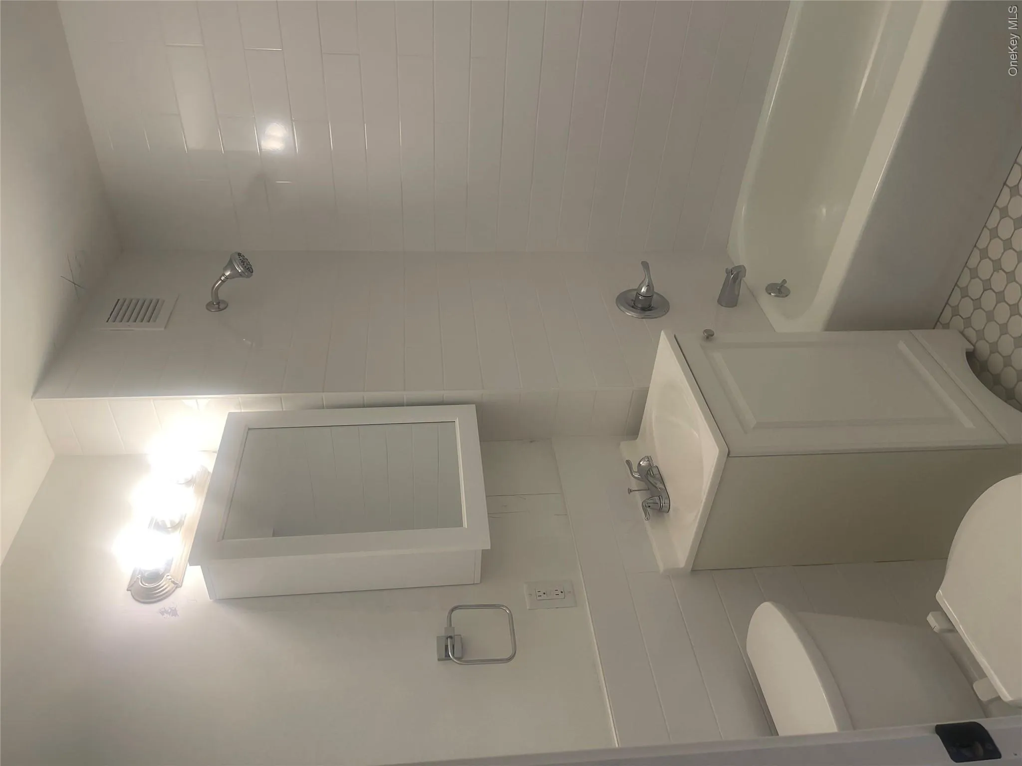 Bathroom featuring a white subway tile surround, white vanity with integrated sink, chrome faucet, and a bathtub with a shower head Bathroom featuring a white subway tile surround, white vanity with integrated sink, chrome faucet, and a bathtub with a shower head