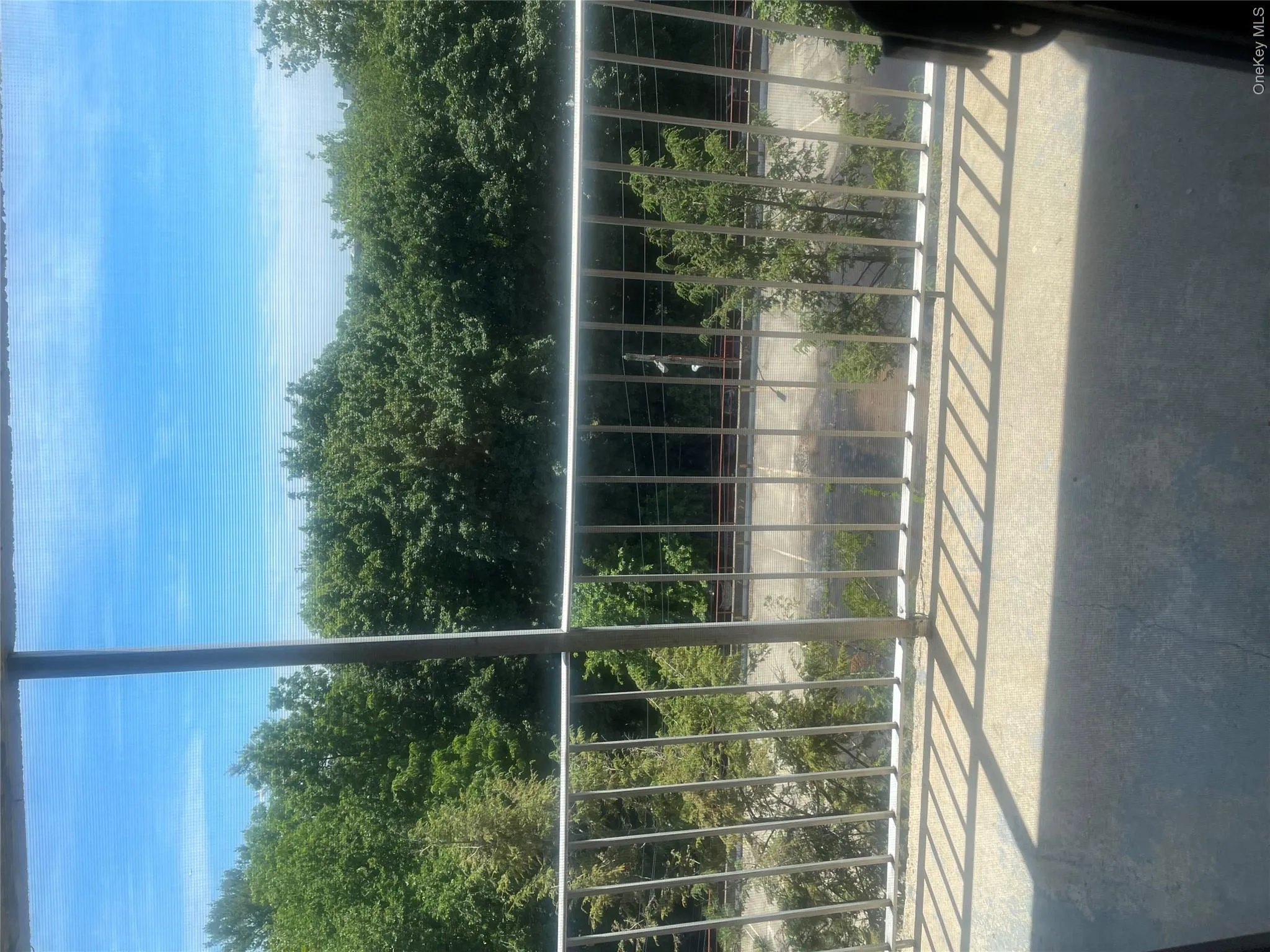 Outdoor balcony with a concrete surface and metal railing overlooking dense tree cover and a railway Outdoor balcony with a concrete surface and metal railing overlooking dense tree cover and a railway
