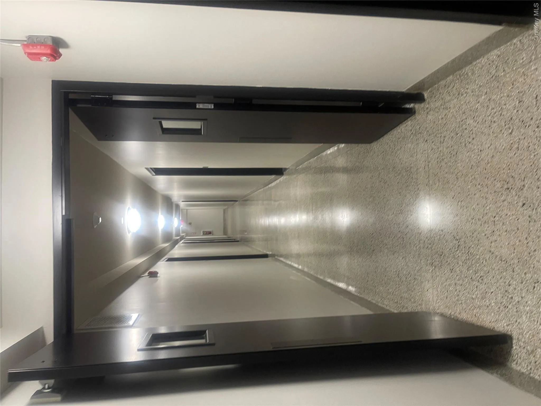 Corridor with polished terrazzo flooring, flush-mounted ceiling lights, white wall finishes, and dark paneled doors Corridor with polished terrazzo flooring, flush-mounted ceiling lights, white wall finishes, and dark paneled doors