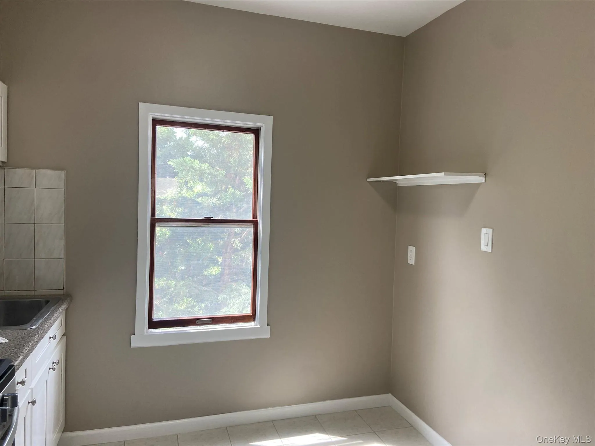 Kitchen area featuring a double-hung window with dark wood framing, white trim, and a white floating shelf Kitchen area featuring a double-hung window with dark wood framing, white trim, and a white floating shelf
