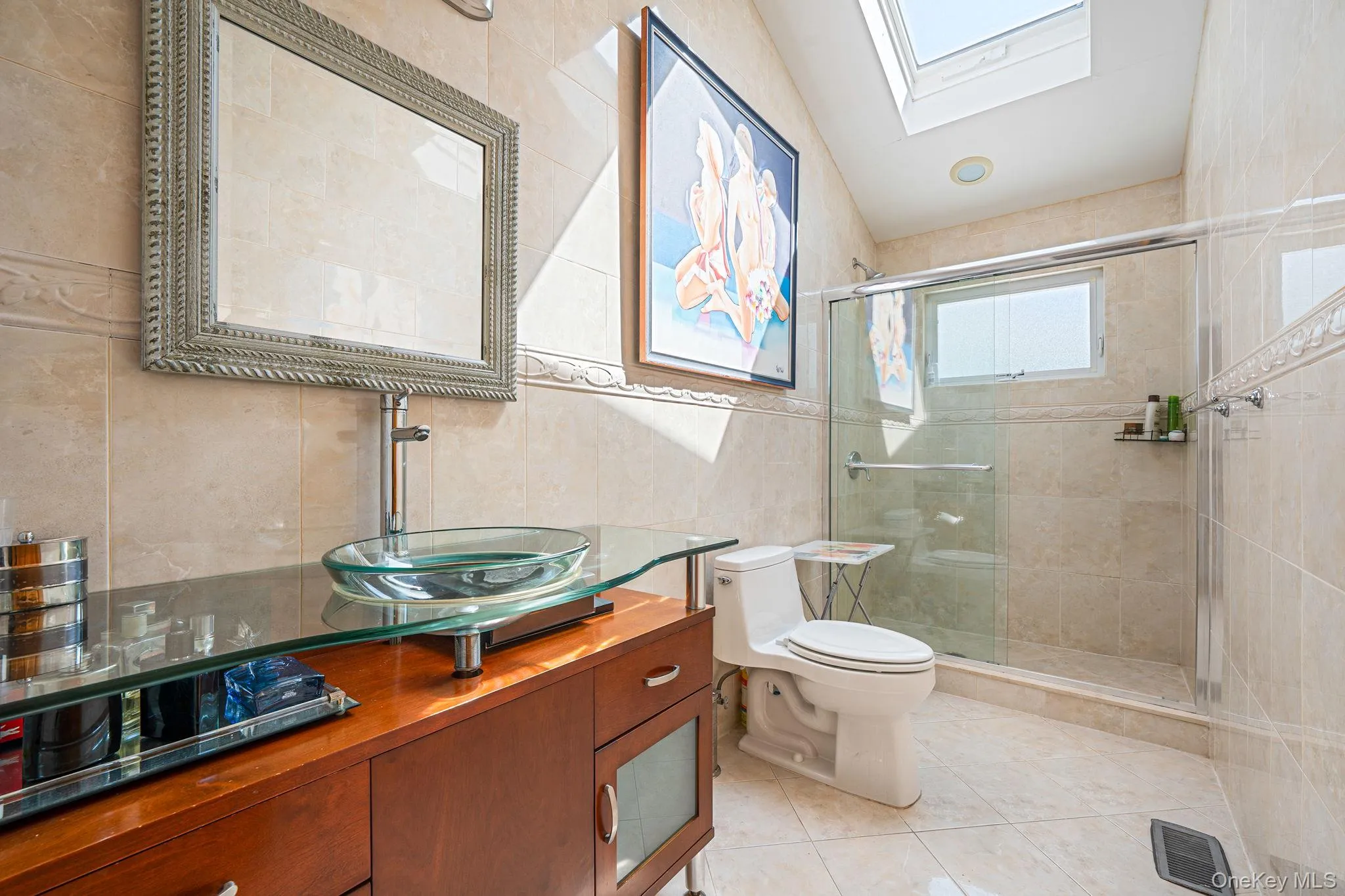 Bathroom featuring tile walls, vanity, a stall shower, a skylight, and light tile patterned floors Bathroom featuring tile walls, vanity, a stall shower, a skylight, and light tile patterned floors