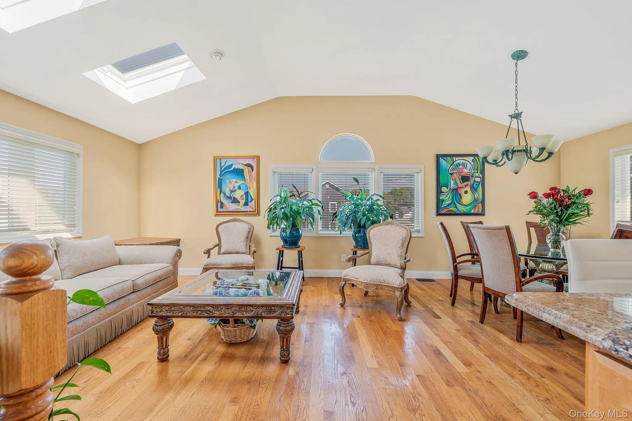 Living room with lofted ceiling, light wood finished floors, a skylight, and a chandelier Living room with lofted ceiling, light wood finished floors, a skylight, and a chandelier