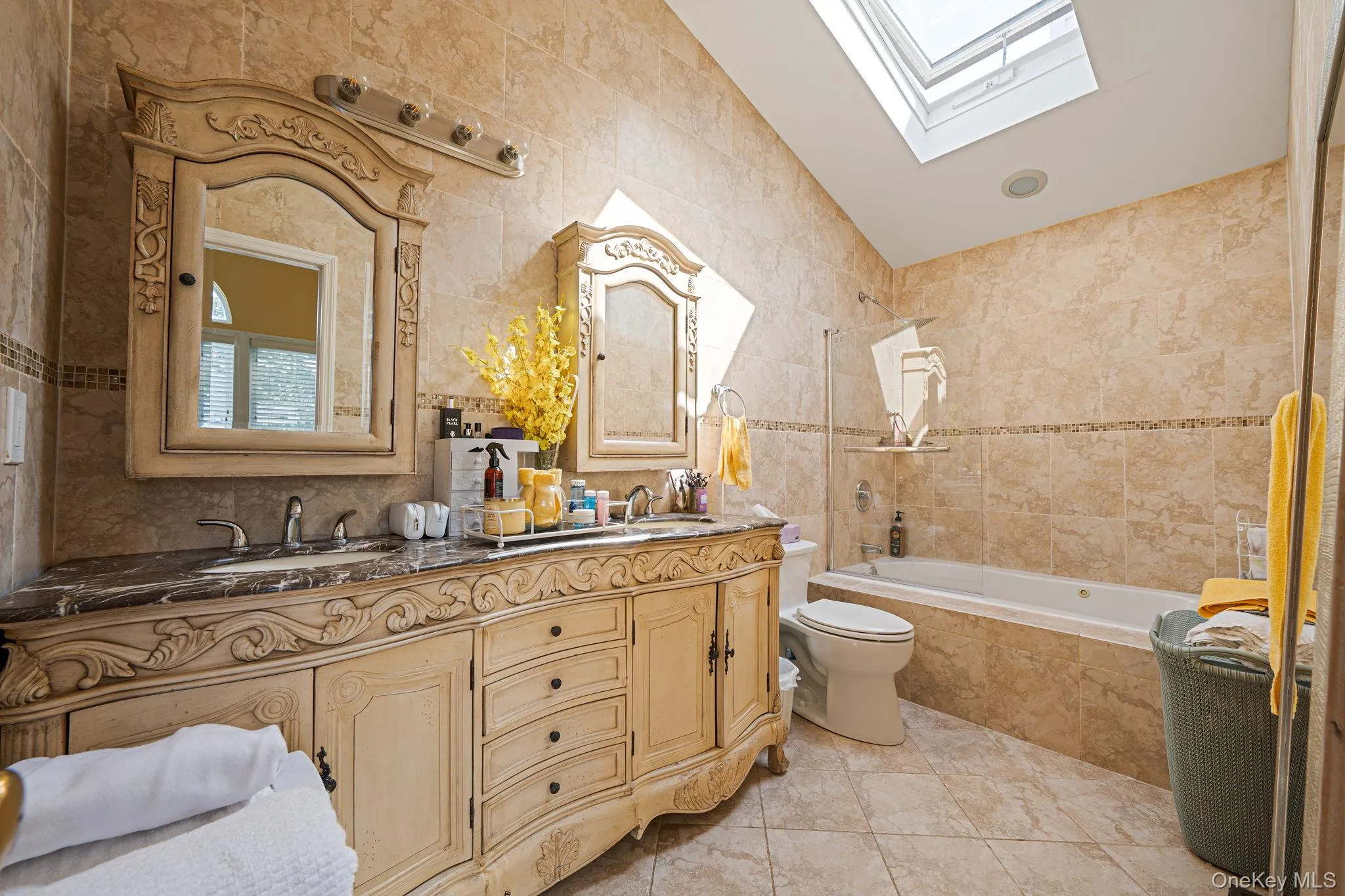 Bathroom featuring tile walls, a skylight, tiled shower / bath, double vanity, and vaulted ceiling Bathroom featuring tile walls, a skylight, tiled shower / bath, double vanity, and vaulted ceiling