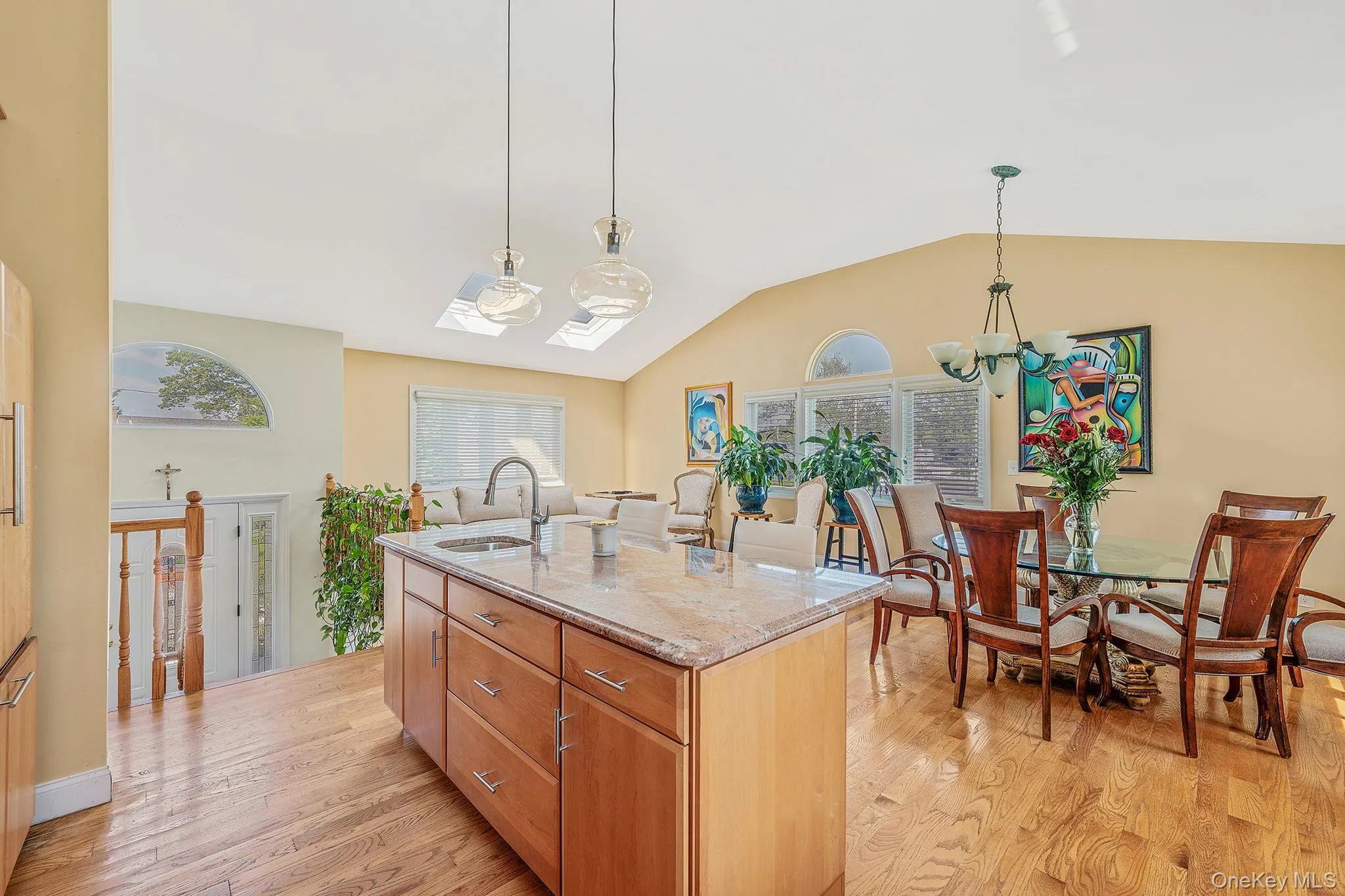Kitchen with light stone counters, pendant lighting, light wood-style flooring, a kitchen island with sink, and a chandelier Kitchen with light stone counters, pendant lighting, light wood-style flooring, a kitchen island with sink, and a chandelier