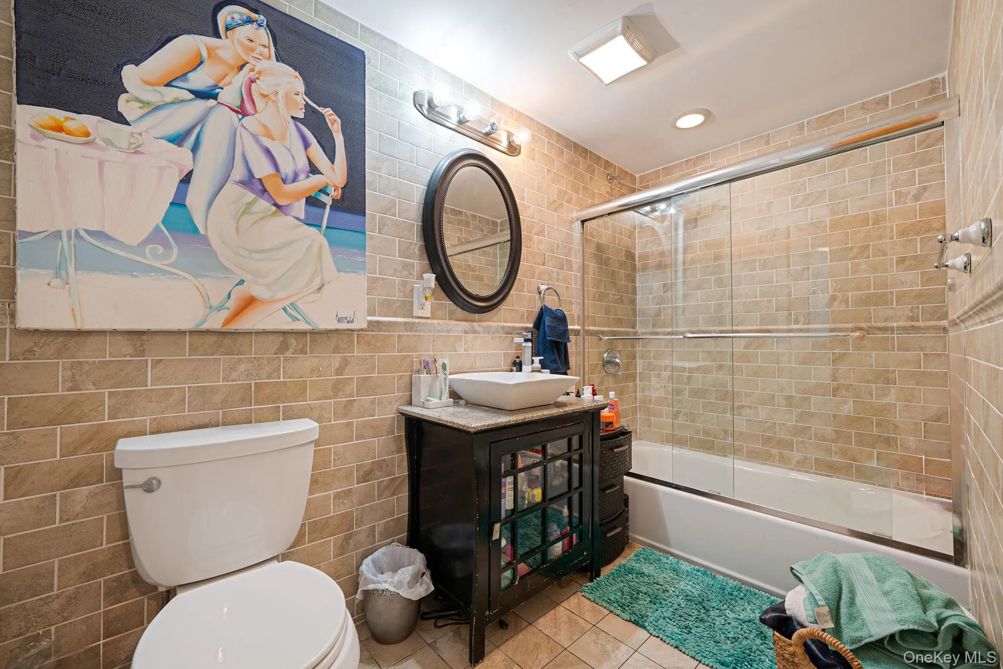 Bathroom with tile walls, shower / bath combination with glass door, vanity, tile patterned floors, and recessed lighting Bathroom with tile walls, shower / bath combination with glass door, vanity, tile patterned floors, and recessed lighting
