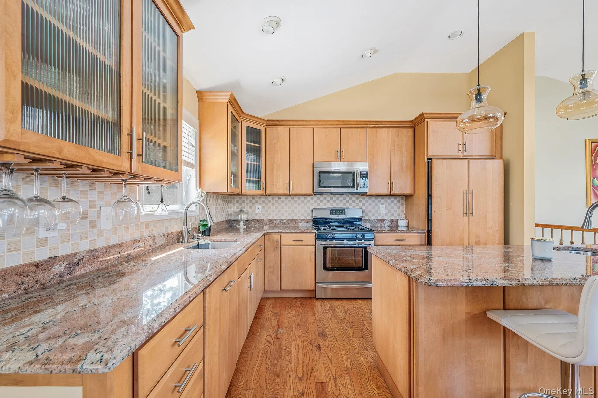 Kitchen with decorative backsplash, a breakfast bar, stainless steel appliances, light wood-style floors, and vaulted ceiling Kitchen with decorative backsplash, a breakfast bar, stainless steel appliances, light wood-style floors, and vaulted ceiling