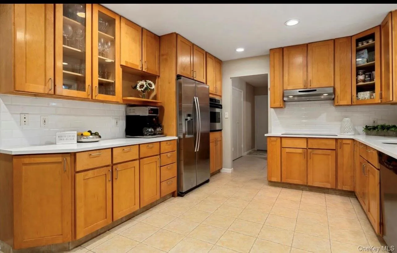 Kitchen featuring stainless steel appliances, tasteful backsplash, brown cabinets, under cabinet range hood, and light countertops Kitchen featuring stainless steel appliances, tasteful backsplash, brown cabinets, under cabinet range hood, and light countertops