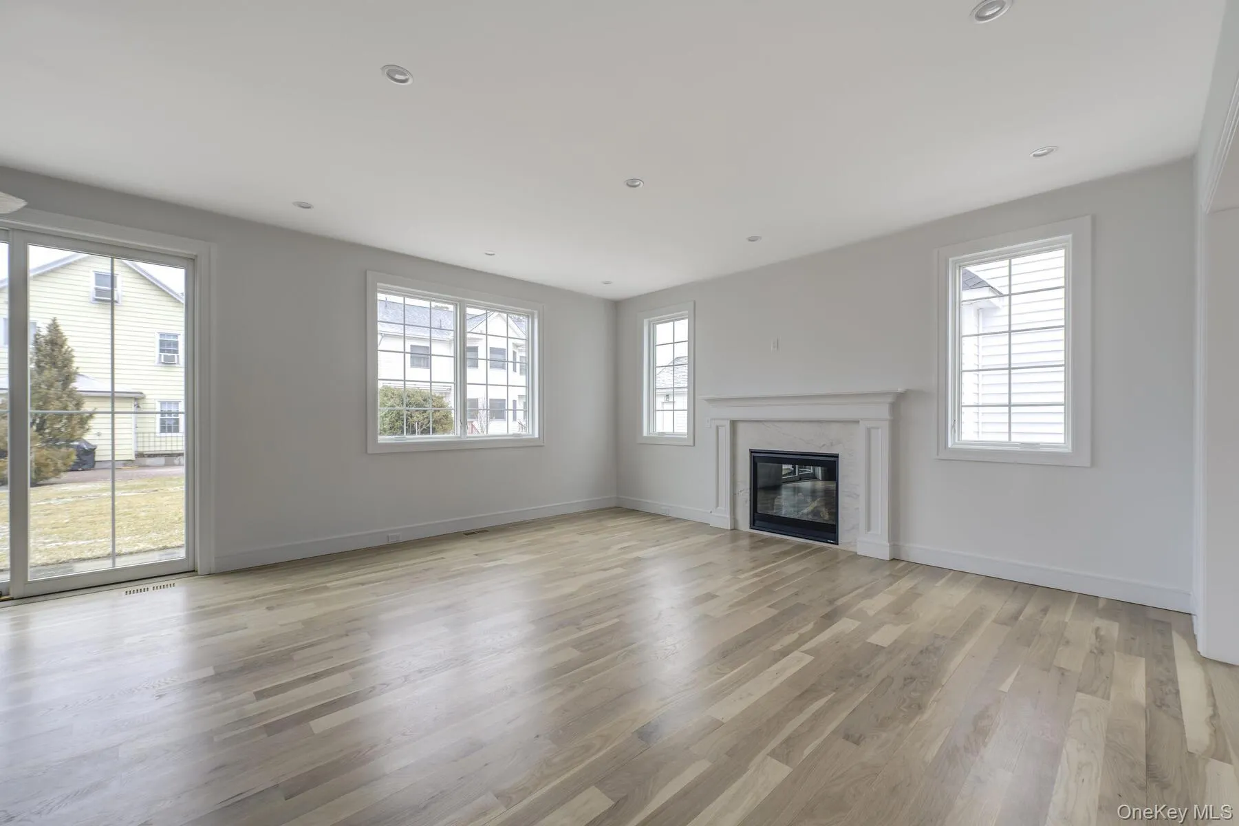 Unfurnished living room featuring light wood-type flooring, a healthy amount of sunlight, a fireplace, and baseboards Unfurnished living room featuring light wood-type flooring, a healthy amount of sunlight, a fireplace, and baseboards