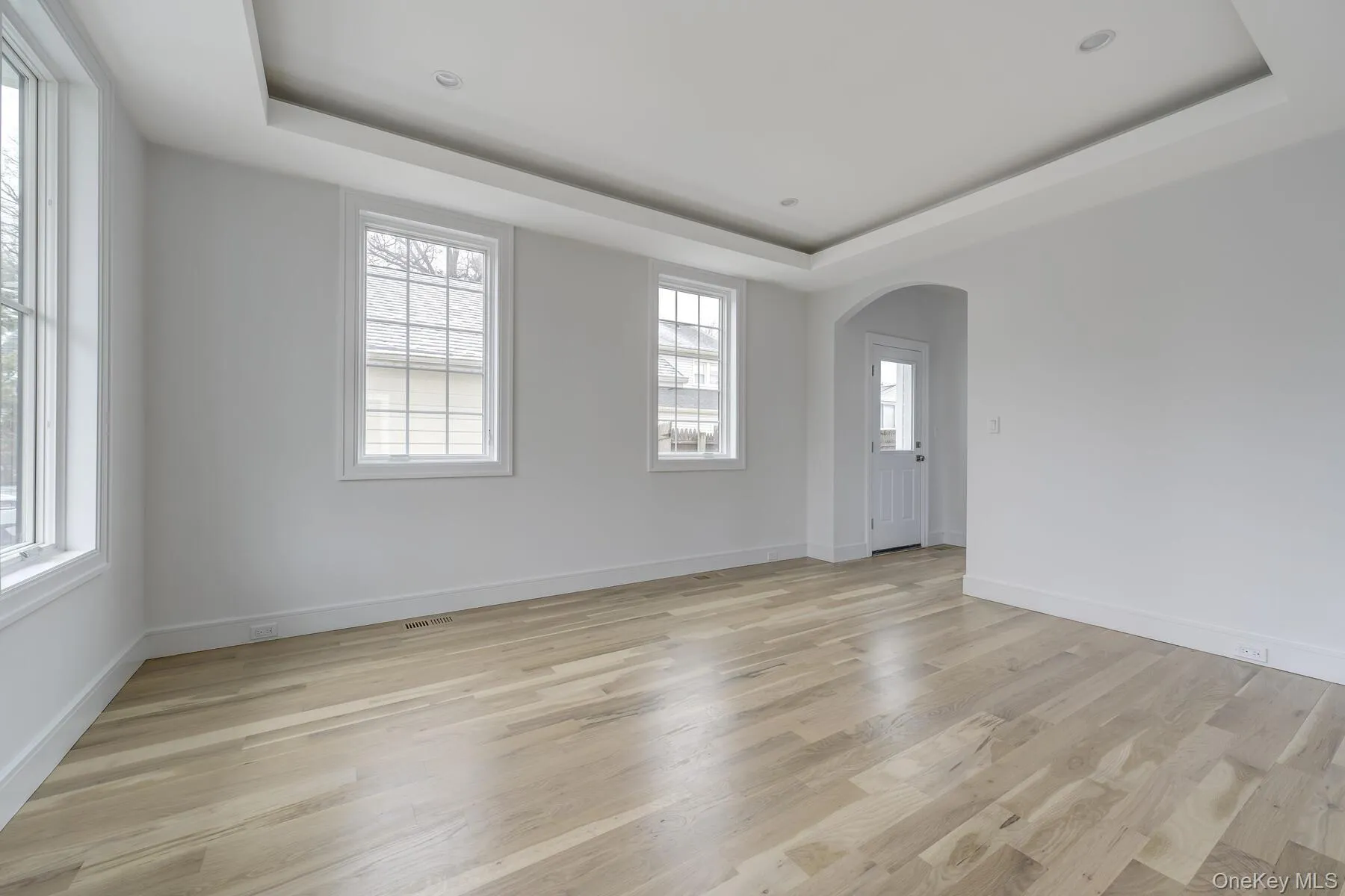 Unfurnished room featuring light wood-type flooring, baseboards, arched walkways, and a raised ceiling Unfurnished room featuring light wood-type flooring, baseboards, arched walkways, and a raised ceiling