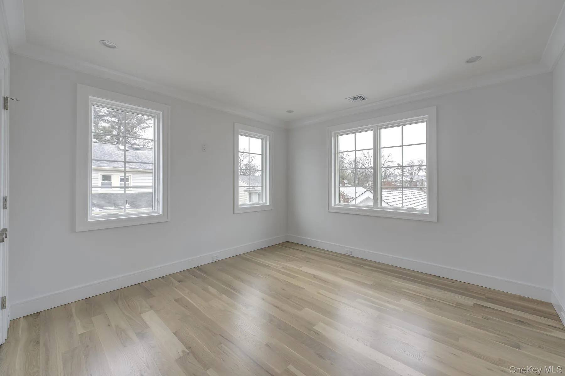 Empty room featuring light wood-type flooring, visible vents, baseboards, and crown molding Empty room featuring light wood-type flooring, visible vents, baseboards, and crown molding