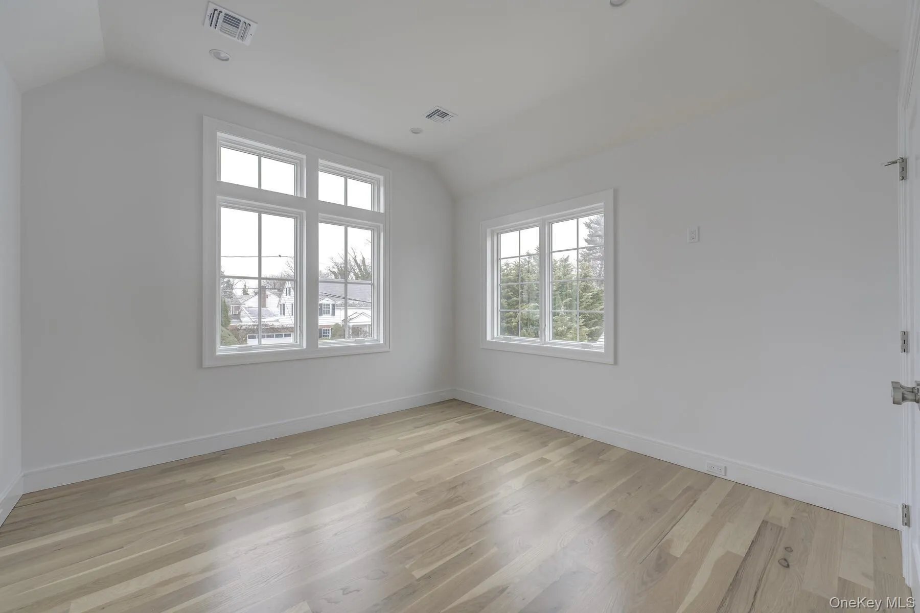 Spare room with lofted ceiling, visible vents, light wood-style flooring, and baseboards Spare room with lofted ceiling, visible vents, light wood-style flooring, and baseboards