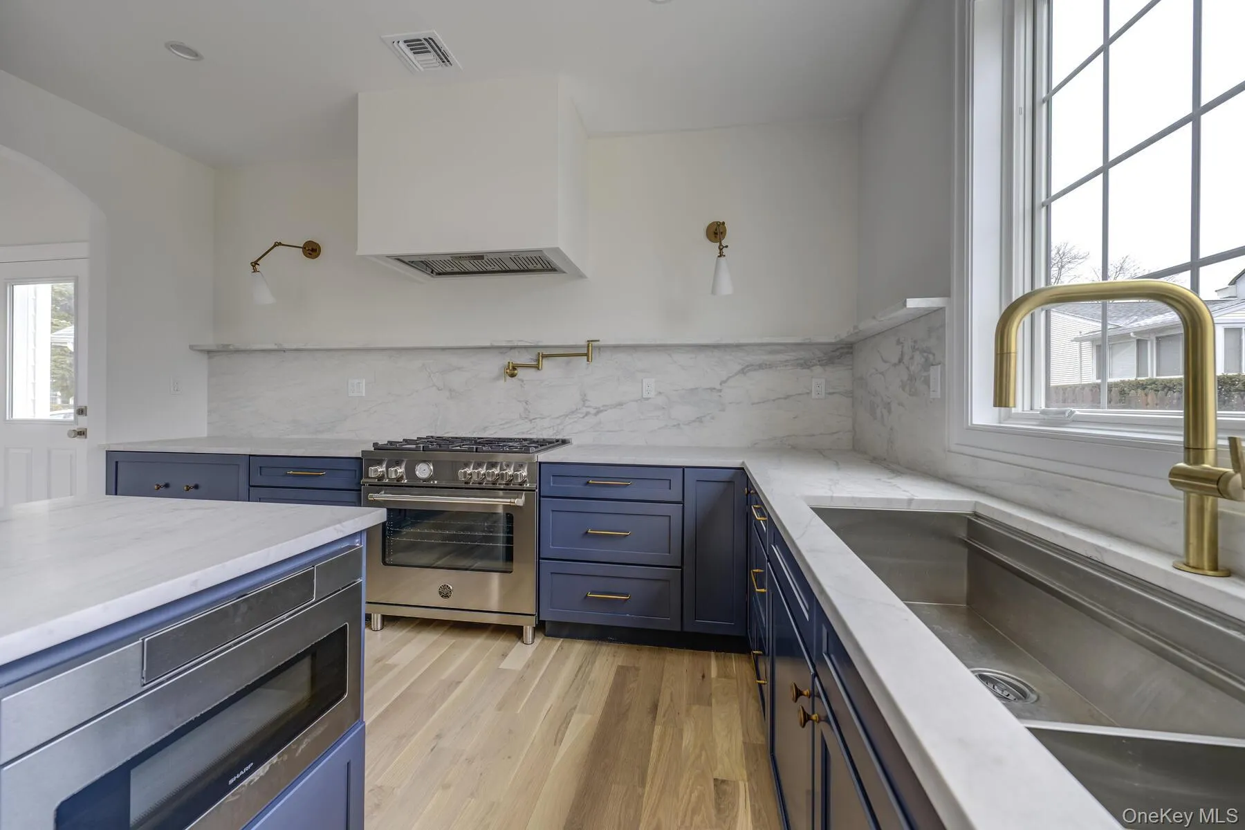 Kitchen featuring light wood-style flooring, a sink, visible vents, appliances with stainless steel finishes, and custom range hood Kitchen featuring light wood-style flooring, a sink, visible vents, appliances with stainless steel finishes, and custom range hood