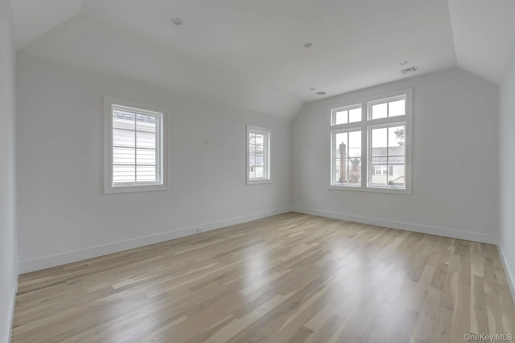 Empty room featuring light wood-style floors, lofted ceiling, visible vents, and baseboards Empty room featuring light wood-style floors, lofted ceiling, visible vents, and baseboards