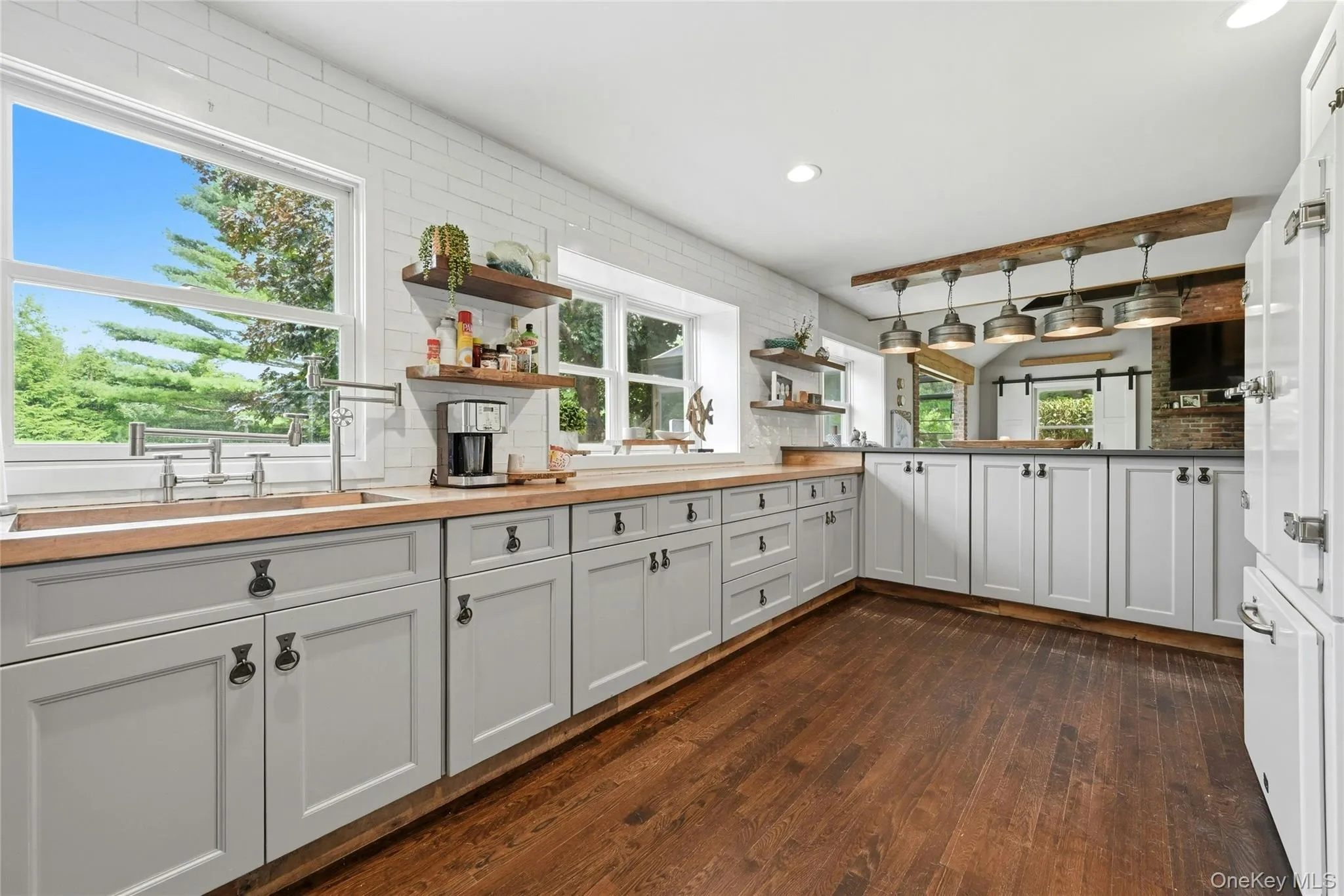 Kitchen featuring wood-finish flooring, light gray cabinetry with dark hardware, butcher block countertops, white subway tile backsplash, and multiple windows Kitchen featuring wood-finish flooring, light gray cabinetry with dark hardware, butcher block countertops, white subway tile backsplash, and multiple windows