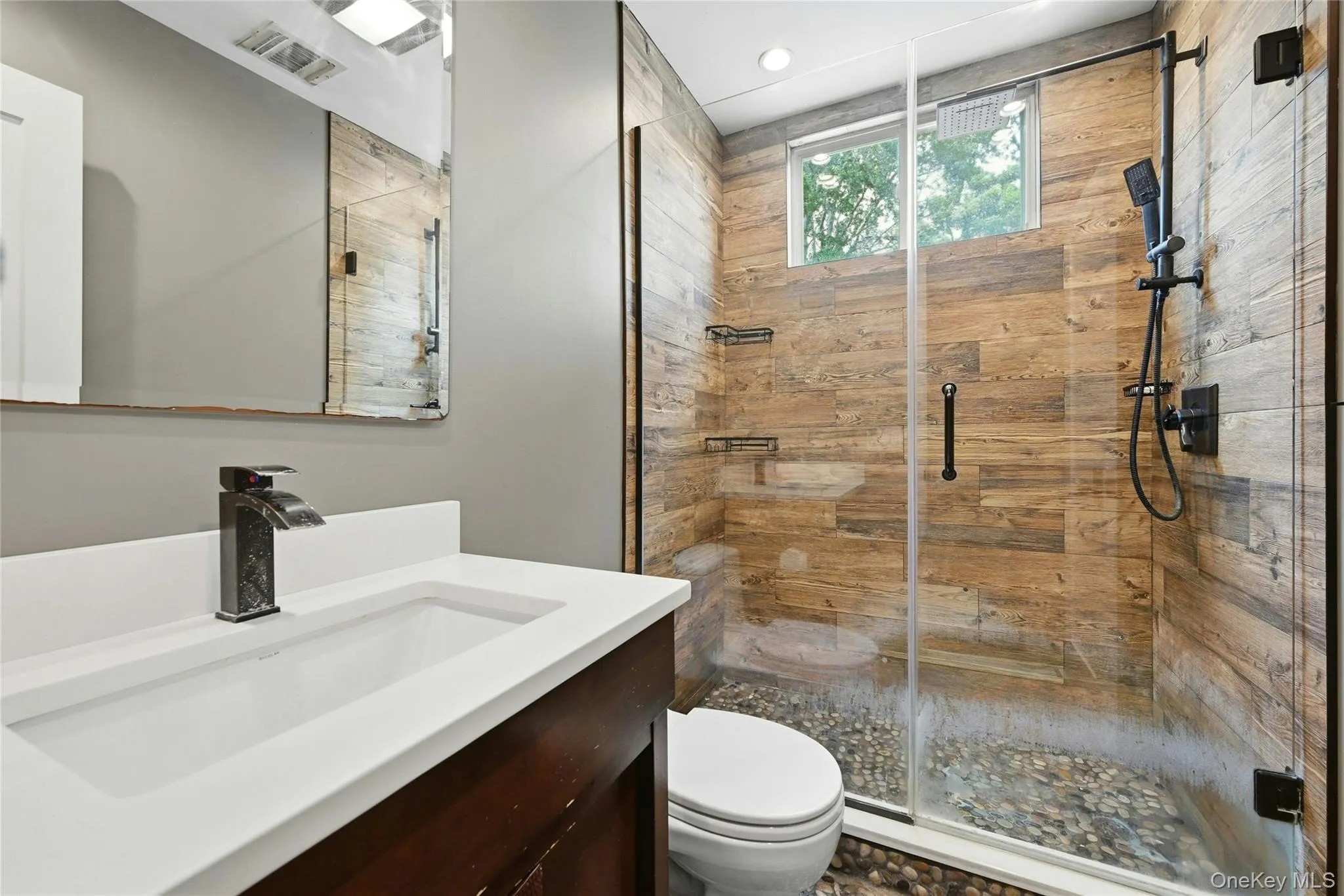 Walk-in shower featuring wood-finish wall tile, pebble floor, and glass enclosure Walk-in shower featuring wood-finish wall tile, pebble floor, and glass enclosure