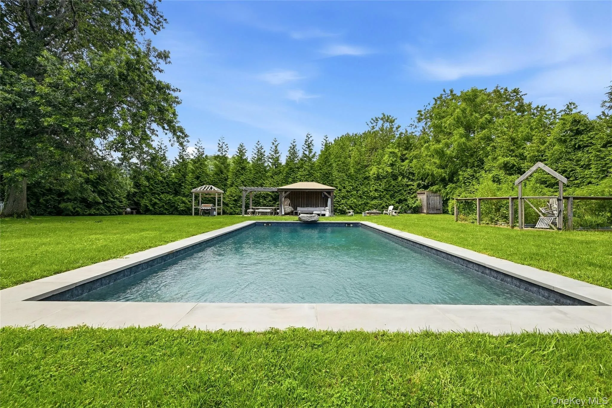 Rectangular swimming pool with a light-colored coping, surrounded by expansive green lawn Rectangular swimming pool with a light-colored coping, surrounded by expansive green lawn
