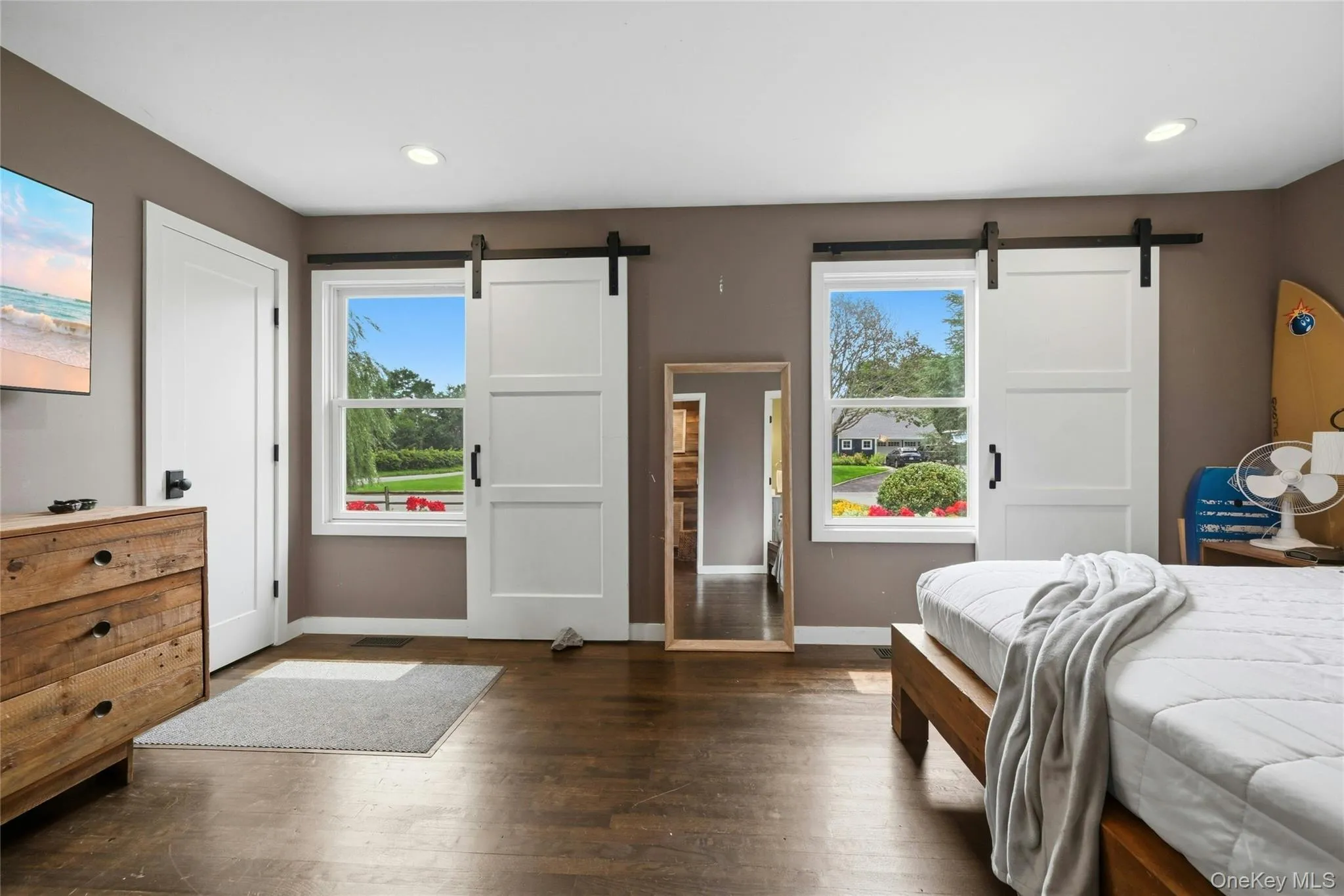 Hardwood-style flooring throughout this space features two windows with barn door style coverings, recessed ceiling lighting, and a solid white interior door Hardwood-style flooring throughout this space features two windows with barn door style coverings, recessed ceiling lighting, and a solid white interior door