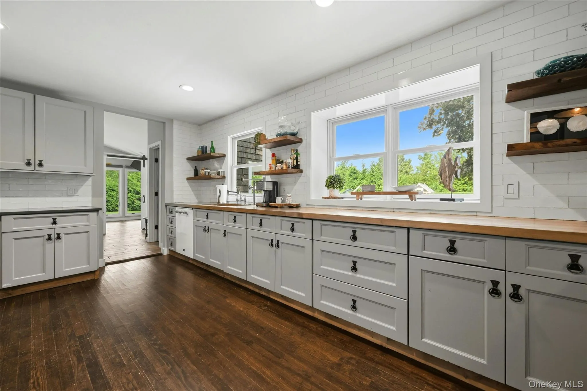 Spacious kitchen featuring gray shaker-style cabinetry with dark hardware, wood-finish countertops, and white subway tile backsplash Spacious kitchen featuring gray shaker-style cabinetry with dark hardware, wood-finish countertops, and white subway tile backsplash