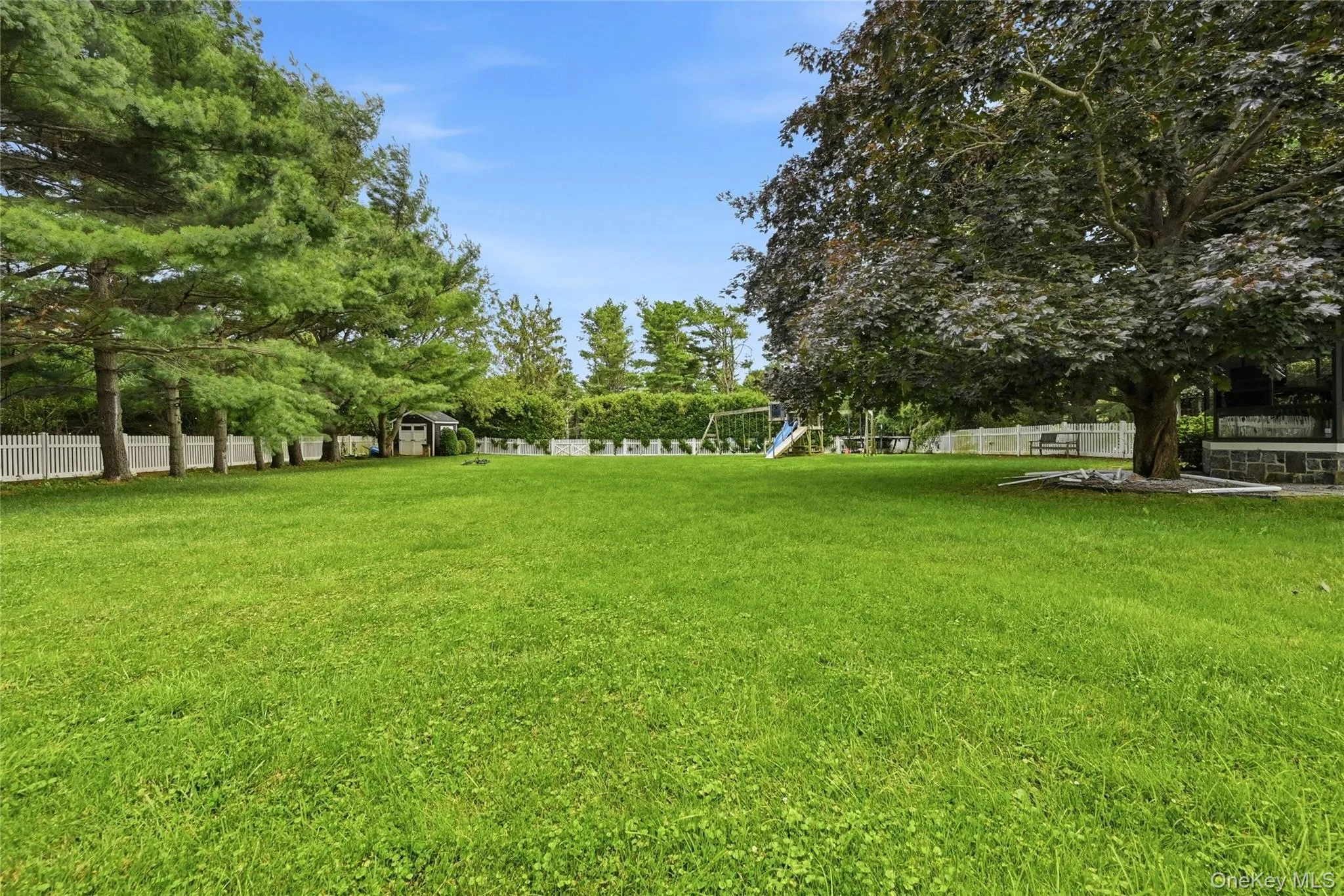 Expansive green lawn framed by mature trees and a white picket fence Expansive green lawn framed by mature trees and a white picket fence