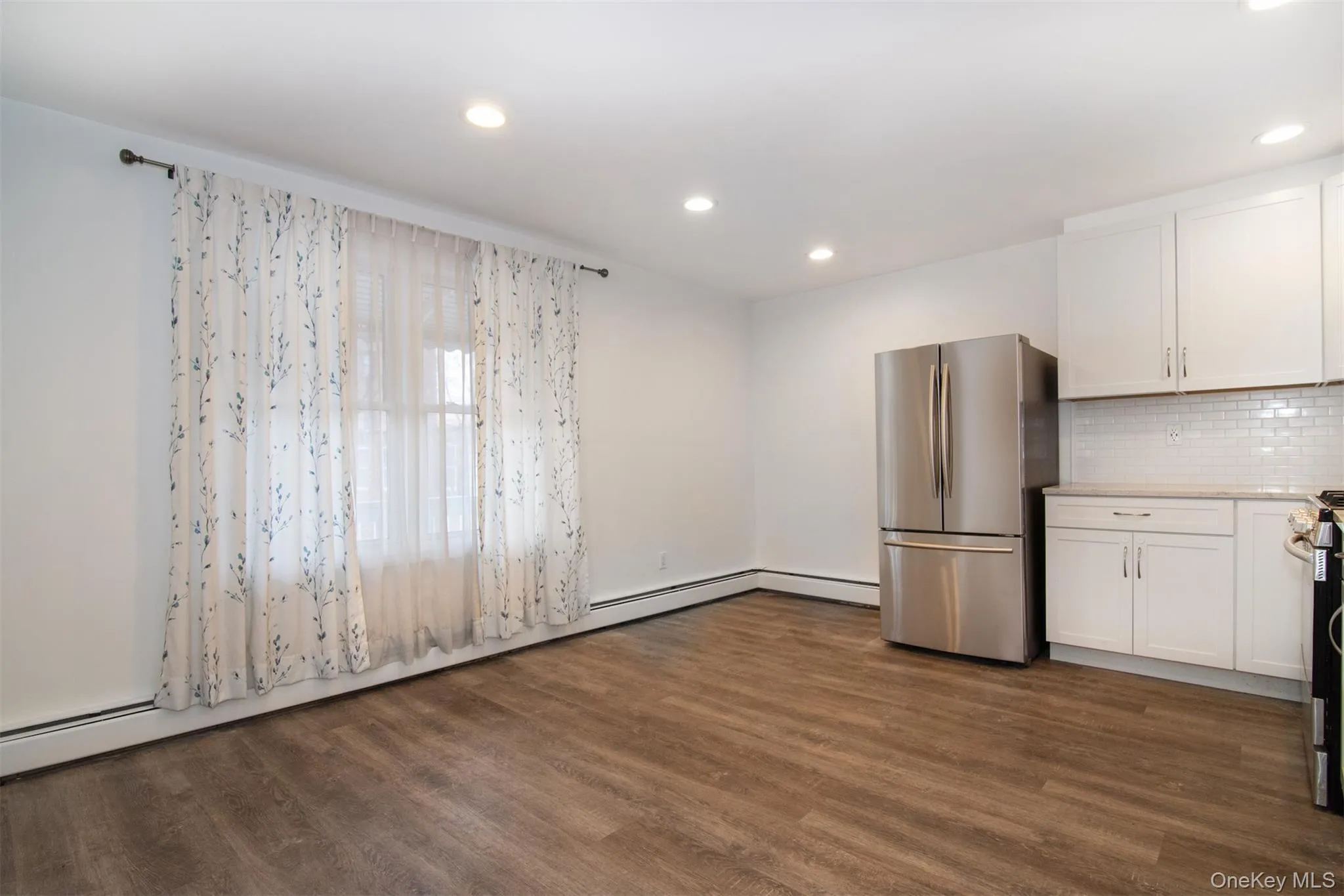 Kitchen featuring white cabinets, stainless steel refrigerator, backsplash, and dark wood-type flooring Kitchen featuring white cabinets, stainless steel refrigerator, backsplash, and dark wood-type flooring