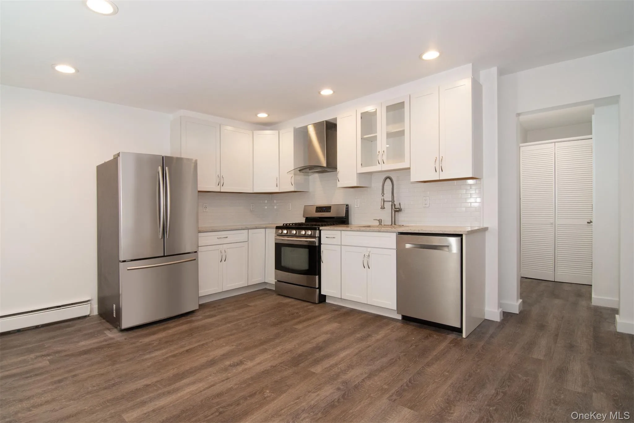 Kitchen with sink, appliances with stainless steel finishes, white cabinets, wall chimney exhaust hood, and dark wood-type flooring Kitchen with sink, appliances with stainless steel finishes, white cabinets, wall chimney exhaust hood, and dark wood-type flooring