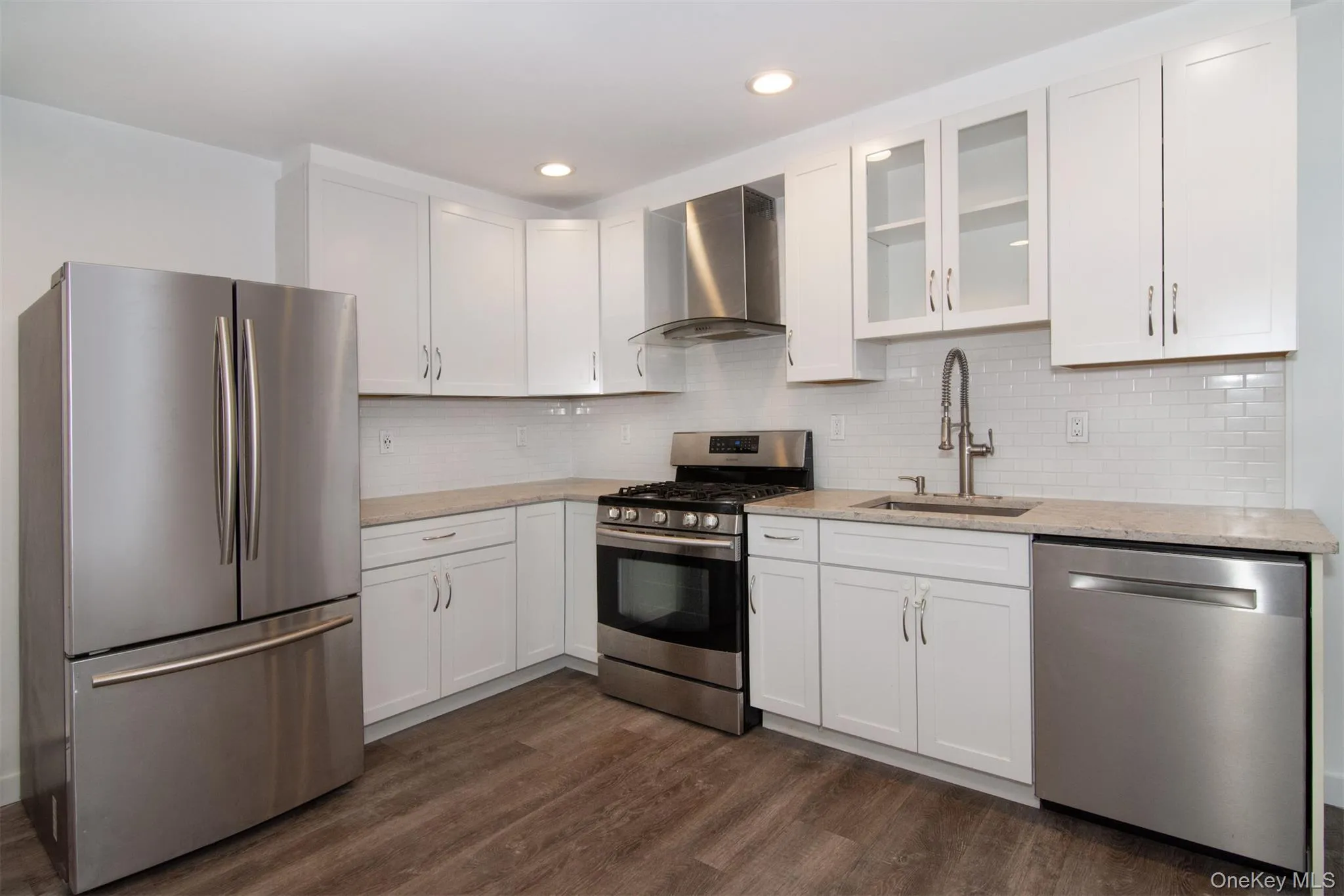 Kitchen featuring appliances with stainless steel finishes, dark hardwood / wood-style flooring, white cabinets, wall chimney range hood, and sink Kitchen featuring appliances with stainless steel finishes, dark hardwood / wood-style flooring, white cabinets, wall chimney range hood, and sink