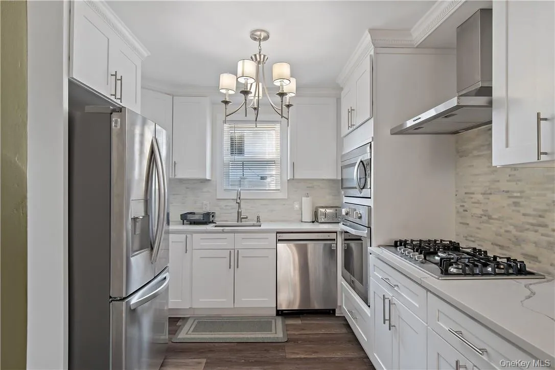 Kitchen featuring decorative backsplash, stainless steel appliances, white cabinets, sink, and wall chimney range hood Kitchen featuring decorative backsplash, stainless steel appliances, white cabinets, sink, and wall chimney range hood