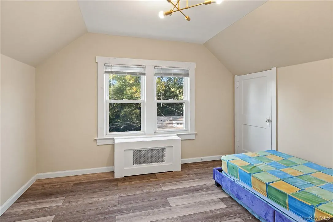 3rd bedroom with lofted ceiling, light hardwood / wood-style floors, an inviting chandelier, and radiator 3rd bedroom with lofted ceiling, light hardwood / wood-style floors, an inviting chandelier, and radiator