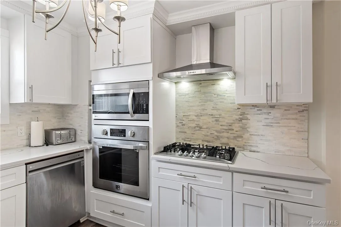 Kitchen with stainless steel appliances, wall chimney range hood, and white cabinetry Kitchen with stainless steel appliances, wall chimney range hood, and white cabinetry