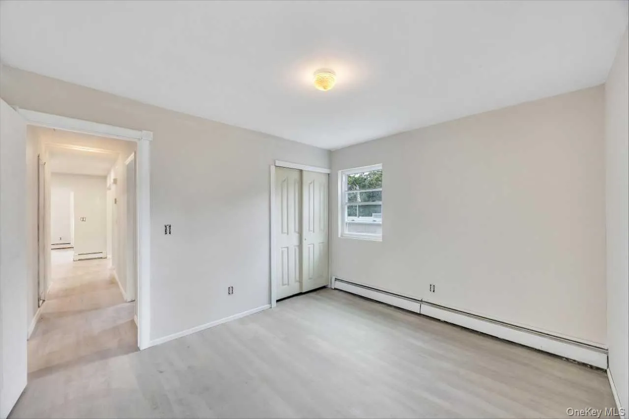 Room featuring light-toned walls, wood-finish flooring, a window providing natural light, and bi-fold closet doors Room featuring light-toned walls, wood-finish flooring, a window providing natural light, and bi-fold closet doors