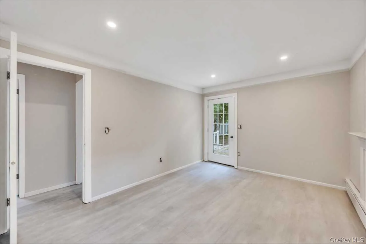 Spacious room featuring wood-finish flooring, recessed lighting, crown molding, and a paneled glass door Spacious room featuring wood-finish flooring, recessed lighting, crown molding, and a paneled glass door