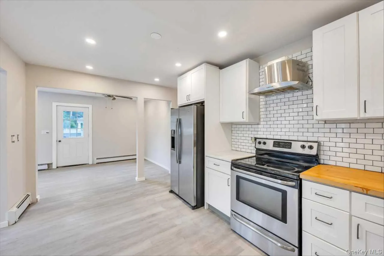 Kitchen featuring stainless steel appliances, white shaker cabinetry with dark pulls, subway tile backsplash, and light wood-finish flooring Kitchen featuring stainless steel appliances, white shaker cabinetry with dark pulls, subway tile backsplash, and light wood-finish flooring