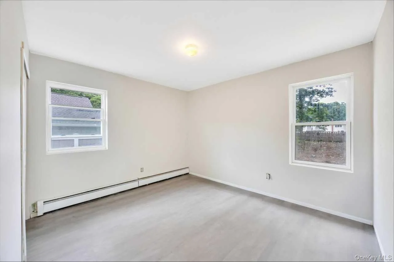 Bright room featuring two windows, light gray walls, wood-finish flooring, and baseboard heating Bright room featuring two windows, light gray walls, wood-finish flooring, and baseboard heating