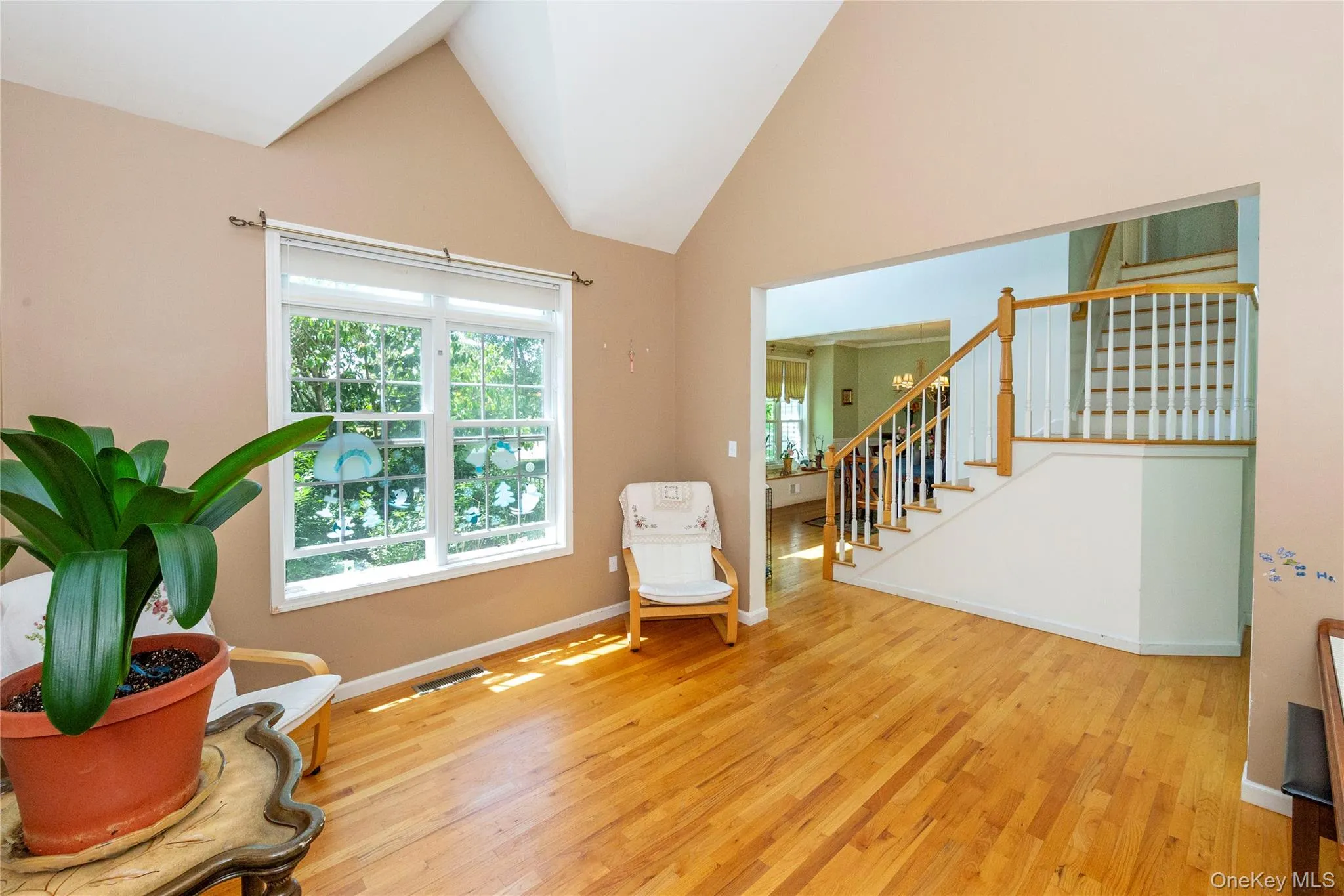 Vaulted ceiling great room with a large multi-pane window, hardwood flooring, and a staircase featuring wood newel posts and banisters with white balusters Vaulted ceiling great room with a large multi-pane window, hardwood flooring, and a staircase featuring wood newel posts and banisters with white balusters