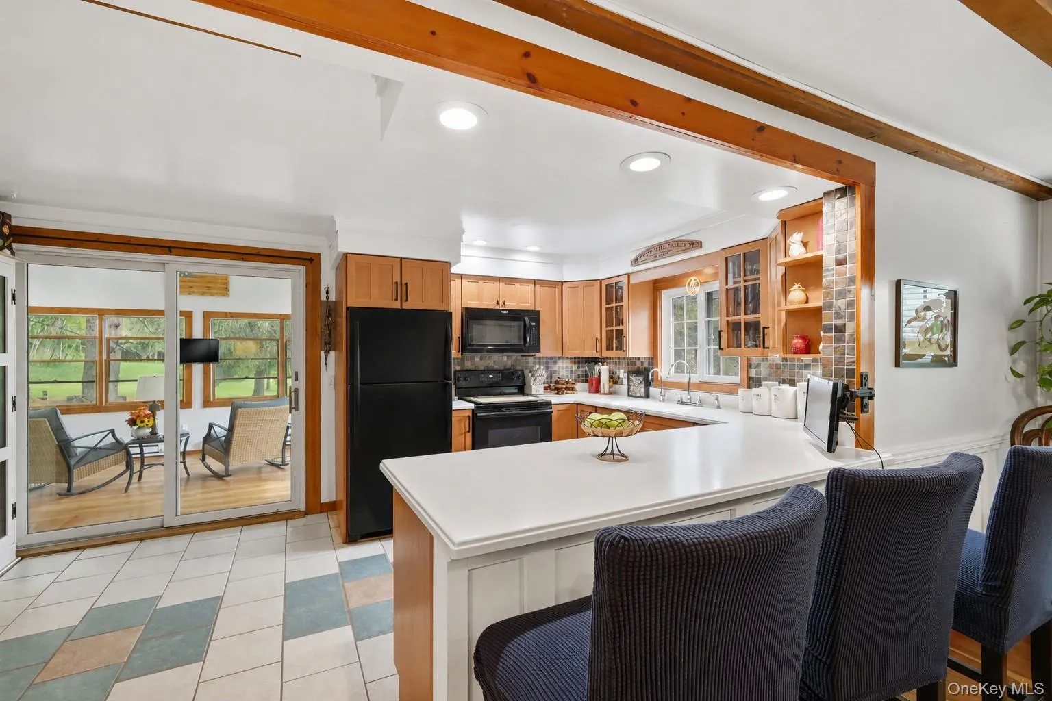A spacious, sunlit kitchen featuring rustic warmth meets modern design, with wood cabinetry, sleek white countertops, and a charming sunroom just beyond. Bright, cozy, and beautifully arranged, the space includes a welcoming island, natural wood trim, and a harmonious blend of functional appliances, decorative accents, and endless greenery visible through large windows. Reverse osmosis faucets in kitchen. A spacious, sunlit kitchen featuring rustic warmth meets modern design, with wood cabinetry, sleek white countertops, and a charming sunroom just beyond. Bright, cozy, and beautifully arranged, the space includes a welcoming island, natural wood trim, and a harmonious blend of functional appliances, decorative accents, and endless greenery visible through large windows. Reverse osmosis faucets in kitchen.