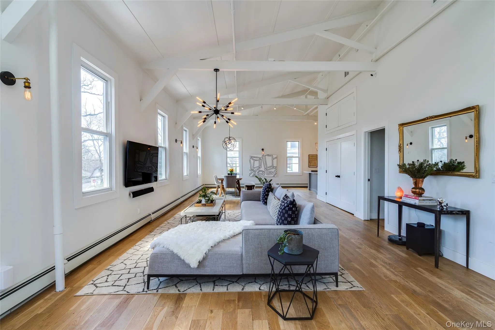 UpperExpansive living area featuring light wood-finish flooring and a high vaulted ceiling with exposed white beams UpperExpansive living area featuring light wood-finish flooring and a high vaulted ceiling with exposed white beams