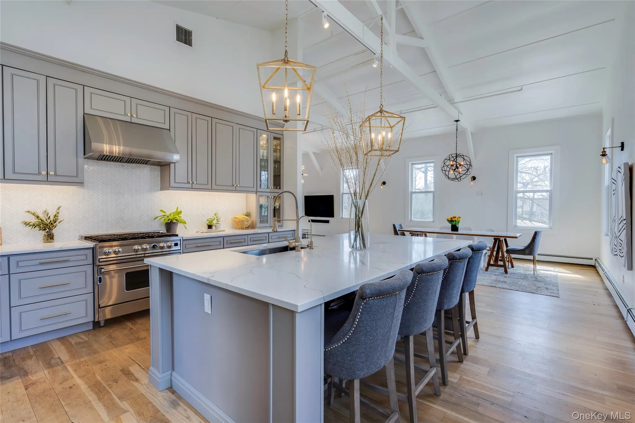 UpperOpen-concept kitchen featuring an oversized island with seating, pendant lighting, stainless steel appliances, and wood-finish flooring UpperOpen-concept kitchen featuring an oversized island with seating, pendant lighting, stainless steel appliances, and wood-finish flooring
